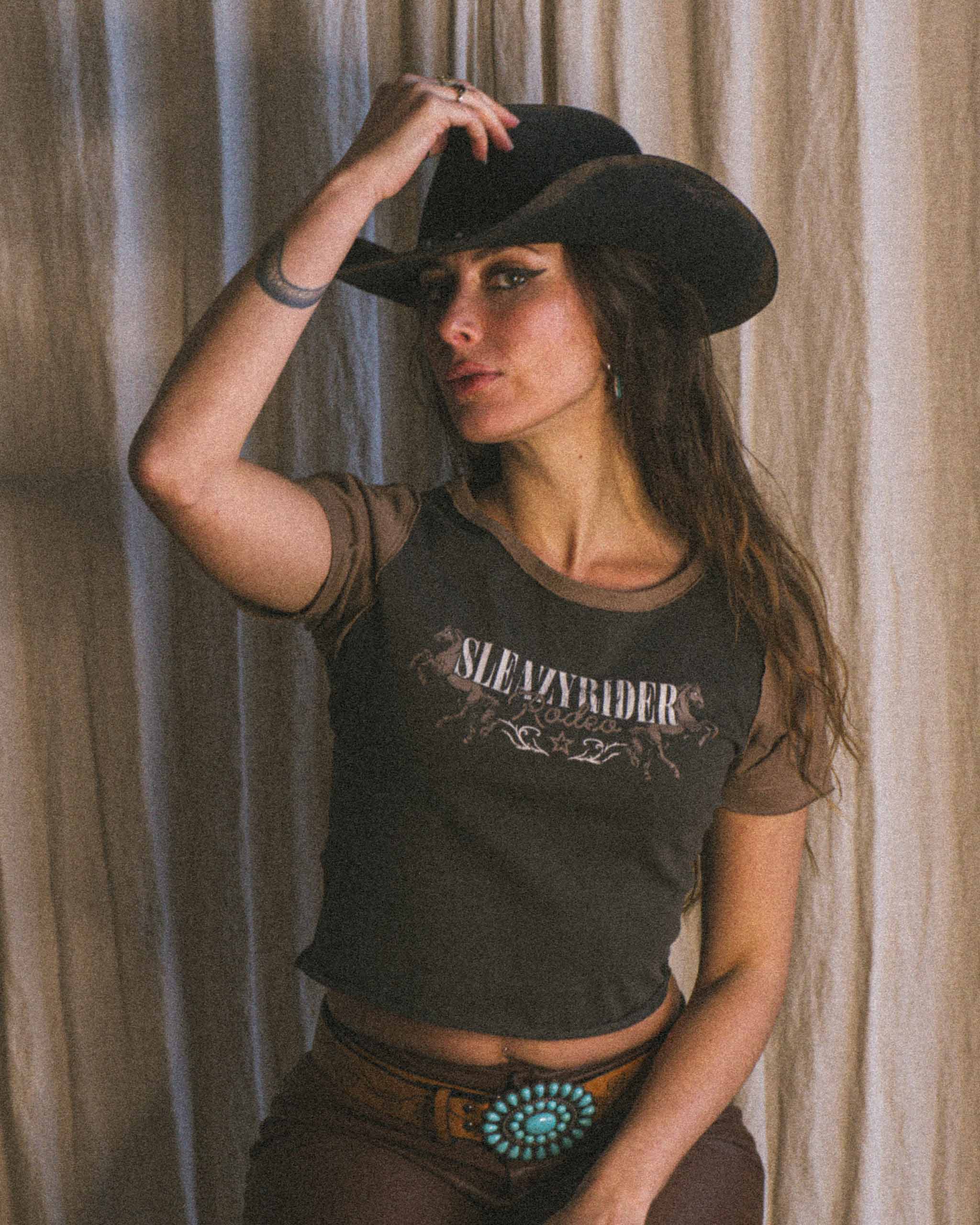 A cowgirl wearing a Sleazy Rider Rodeo baby tee.
