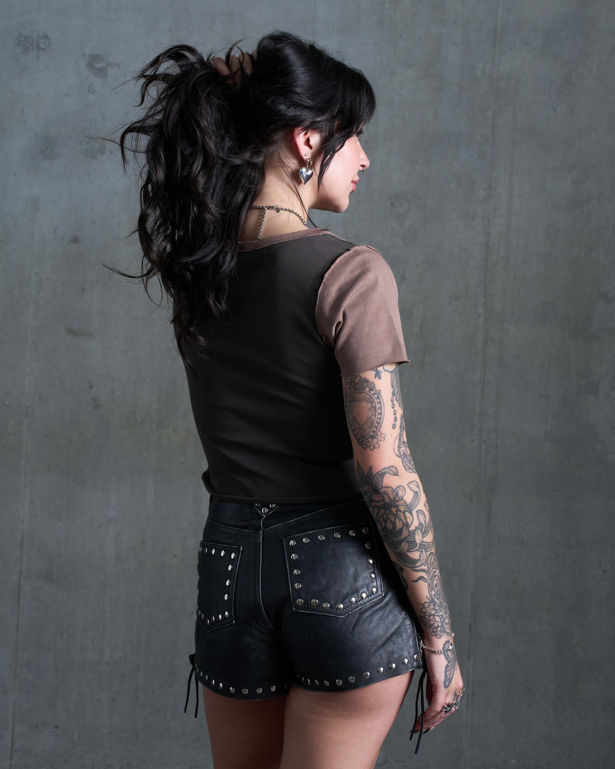 A behind view of an alternative woman wearing a Sleazy Rider dark western baby t-shirt, with studded shorts.