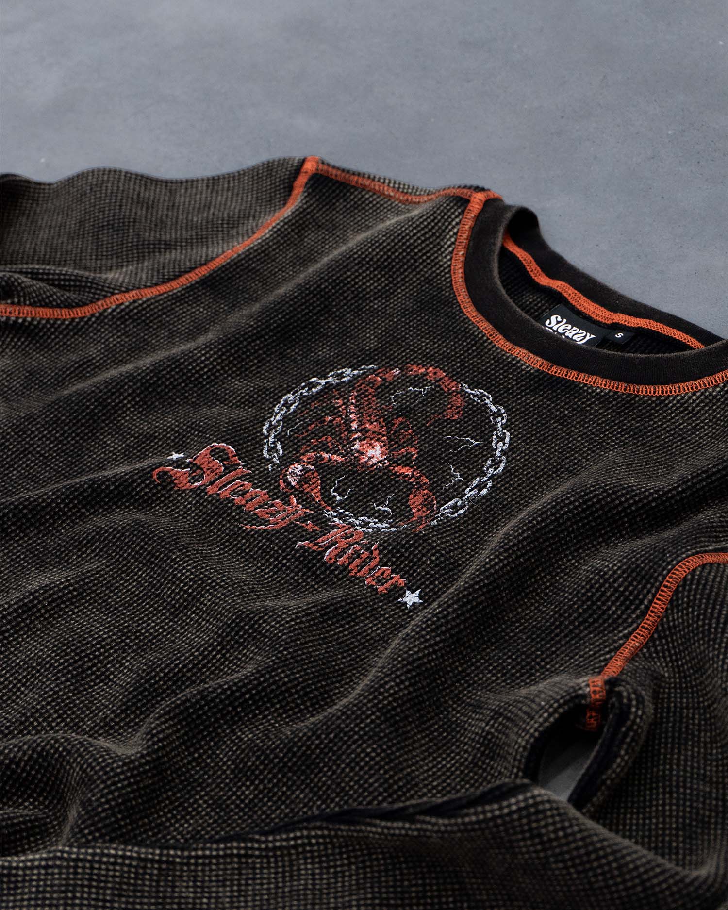 A waffle knit long sleeve top with a heavy acid wash, scorpion screen print and orange contrast stitching, closeup view.