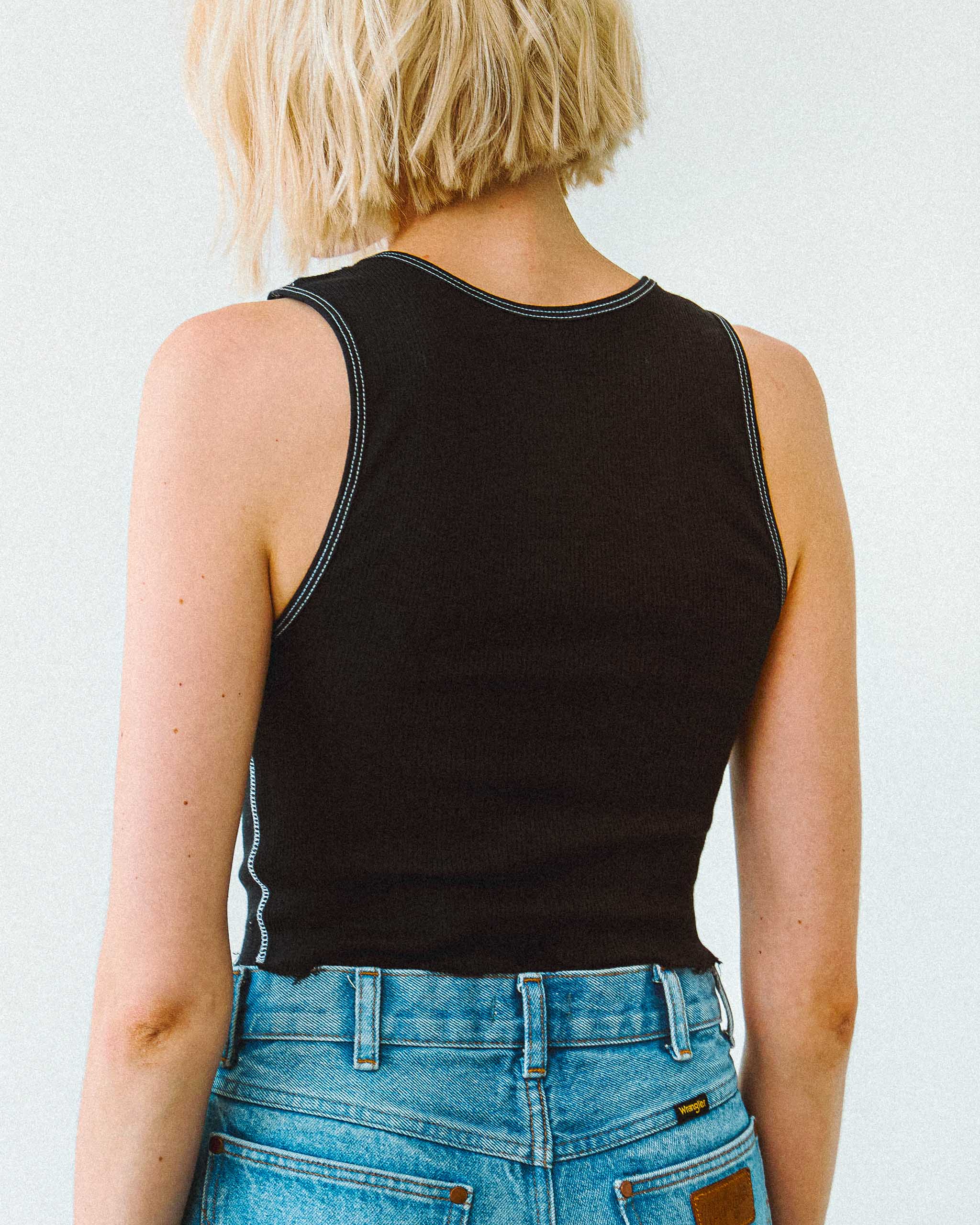 Person wearing a black tank top and blue jeans against a white background.