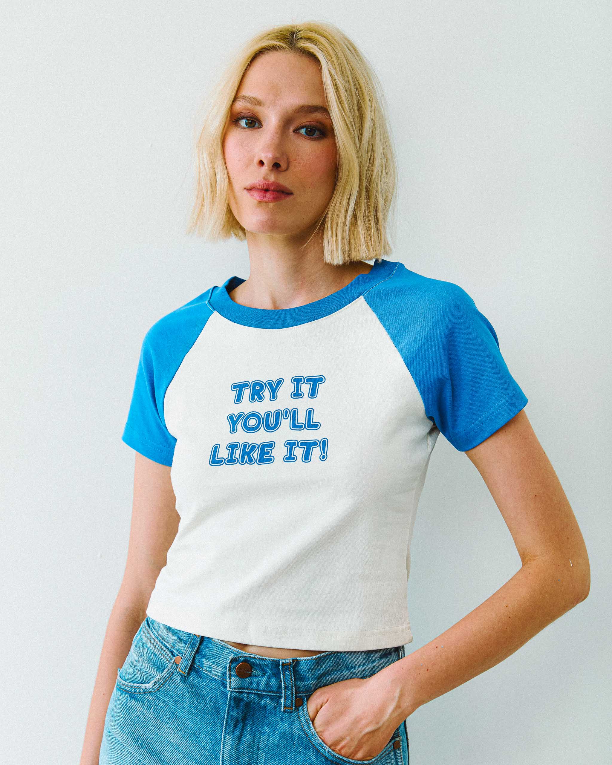 Model wearing a blue and white "Try it you'll like it!" slogan raglan vintage style baby t-shirt, standing against a plain background.