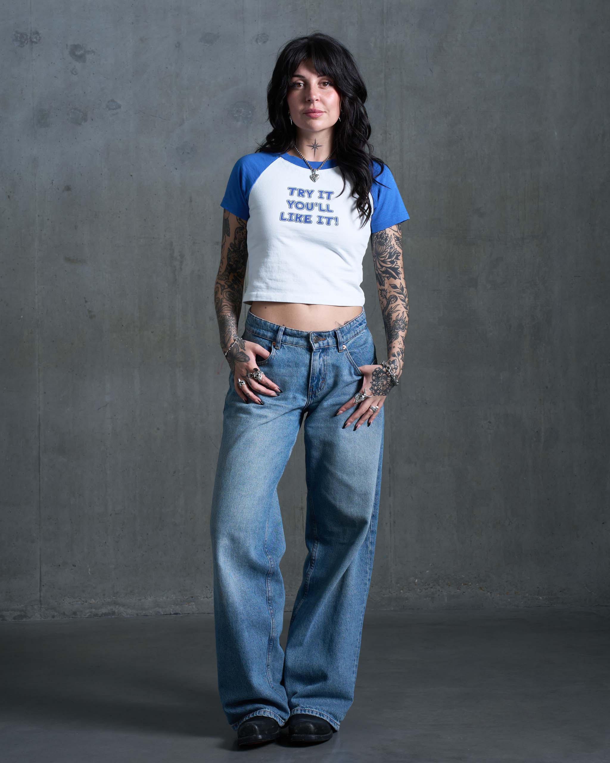 An alt model wearing a blue and white "Try it you'll like it!" slogan raglan vintage baby t-shirt and low-rise jeans.