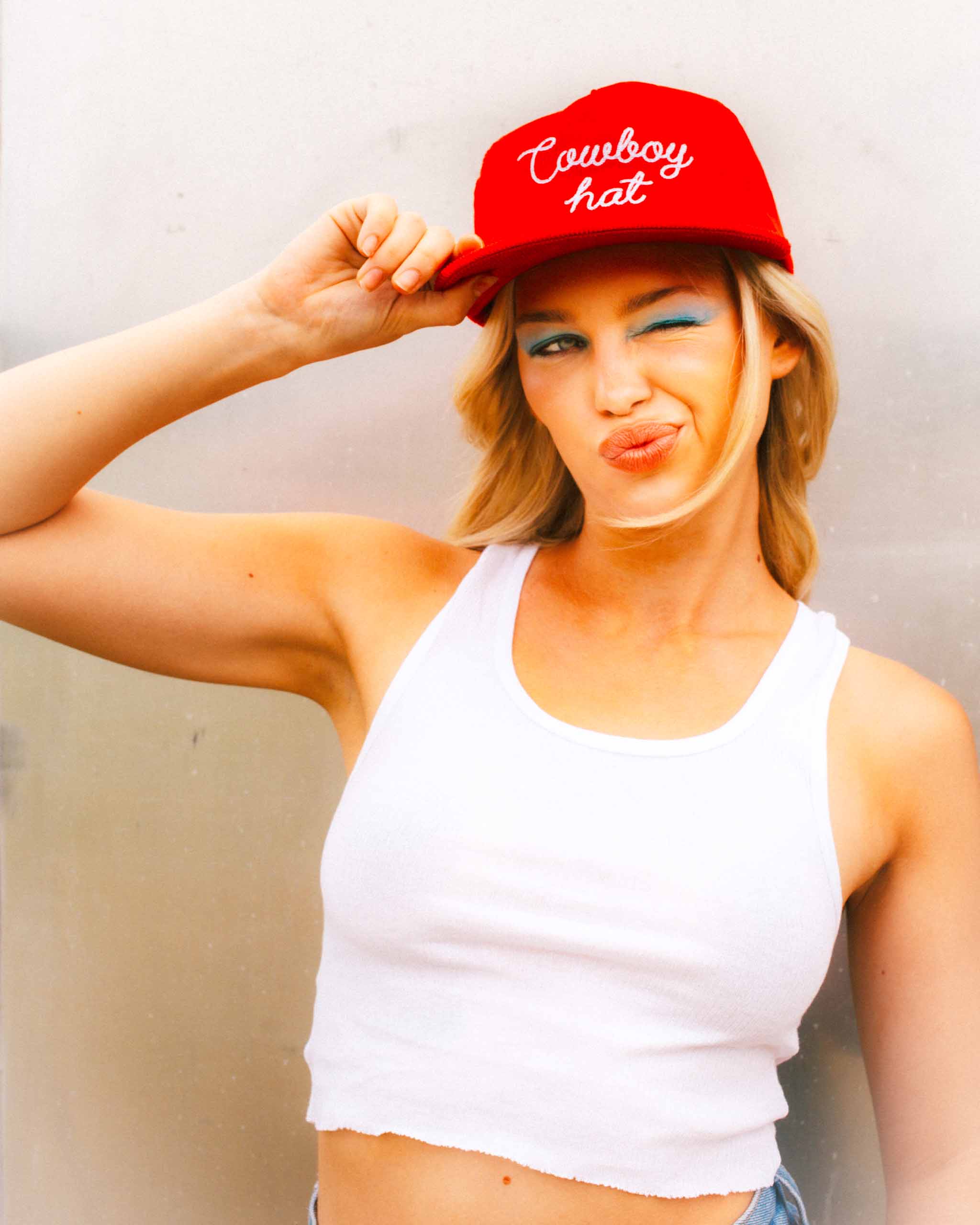 Woman wearing a red corduroy cap with 'Cowboy hat' text, posing against a plain background