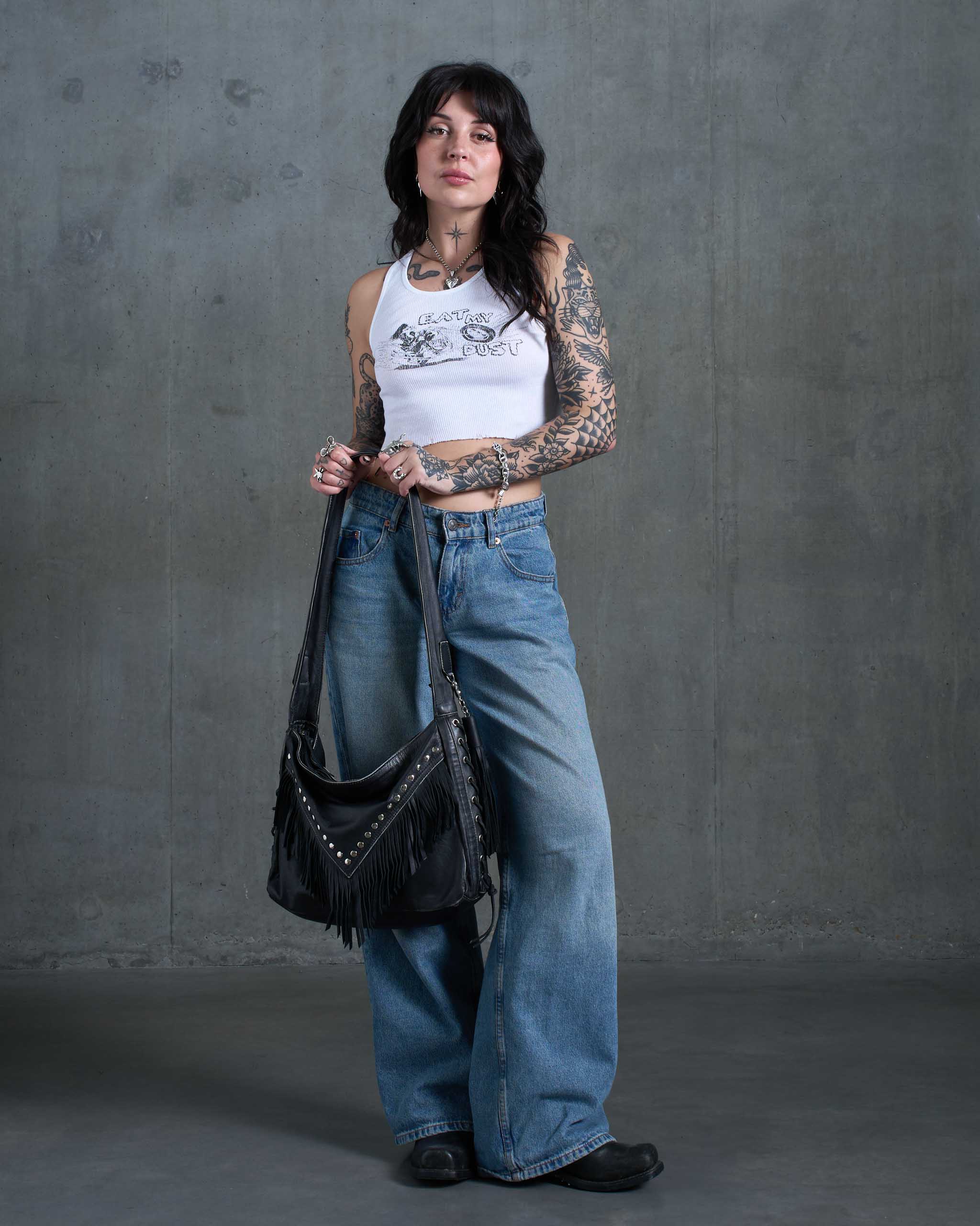 A tattooed model holding a large gothic western slouchy leather bag.