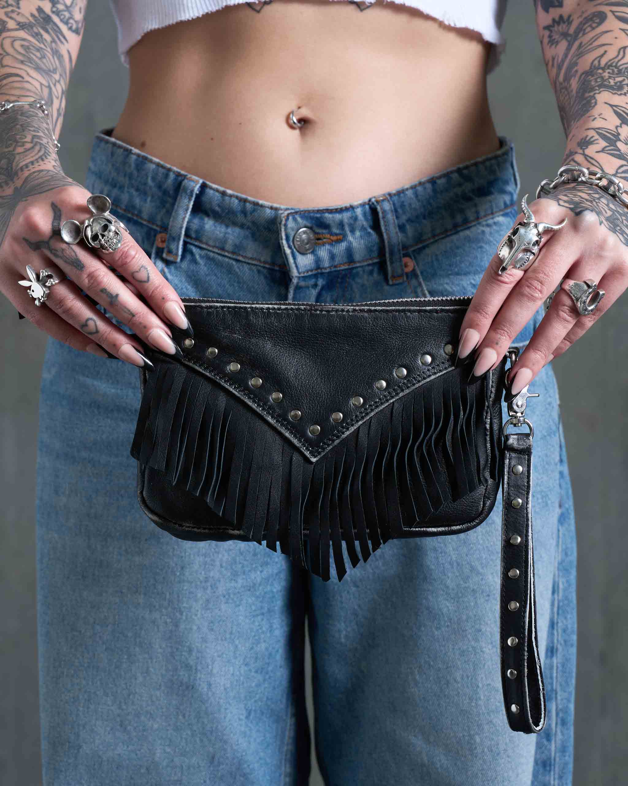 An alternative model holding up a gothic western leather clutch bag, with studs and fringe.