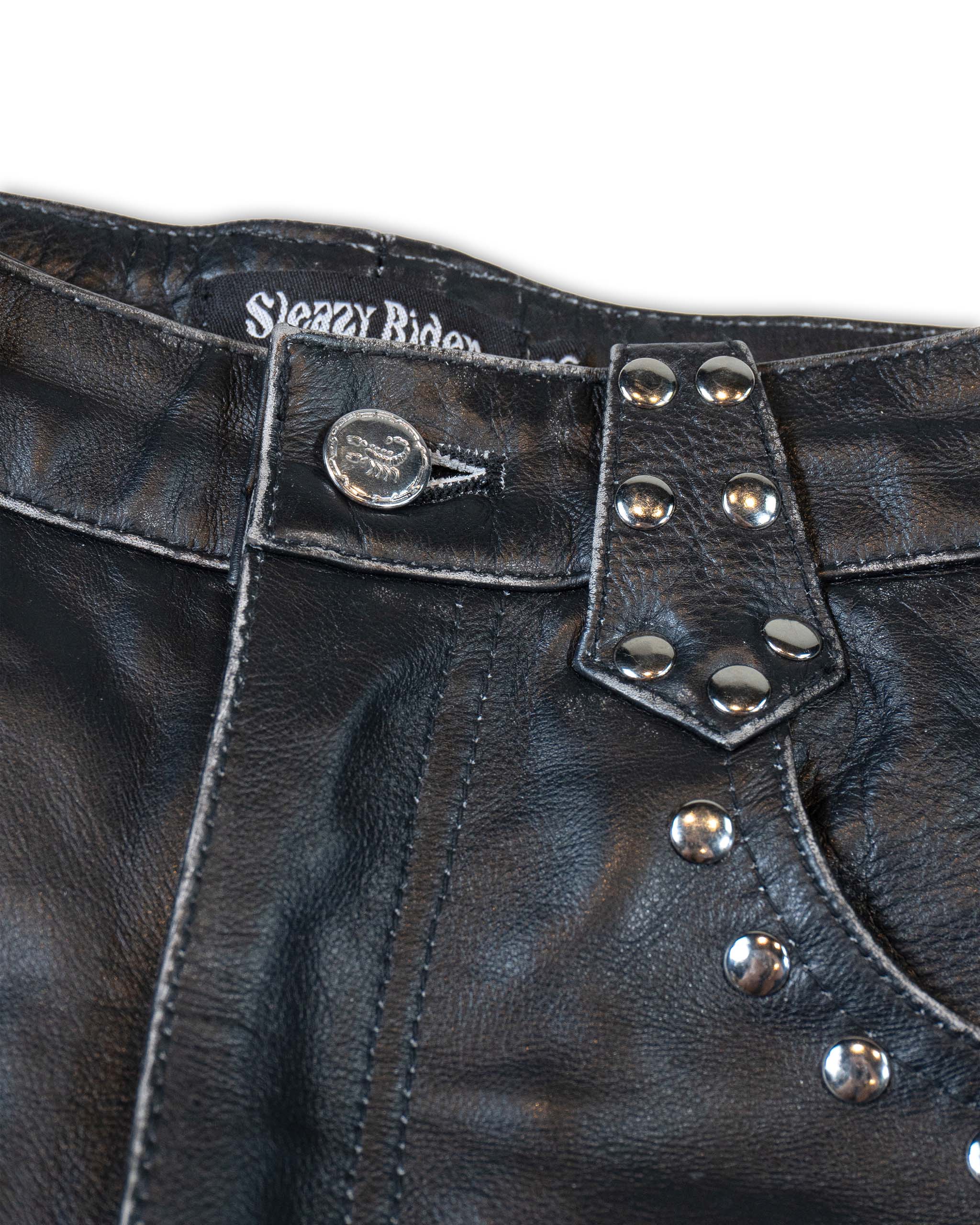 A close up of Sleazy Rider scorpion buttons, seen on studded leather shorts.