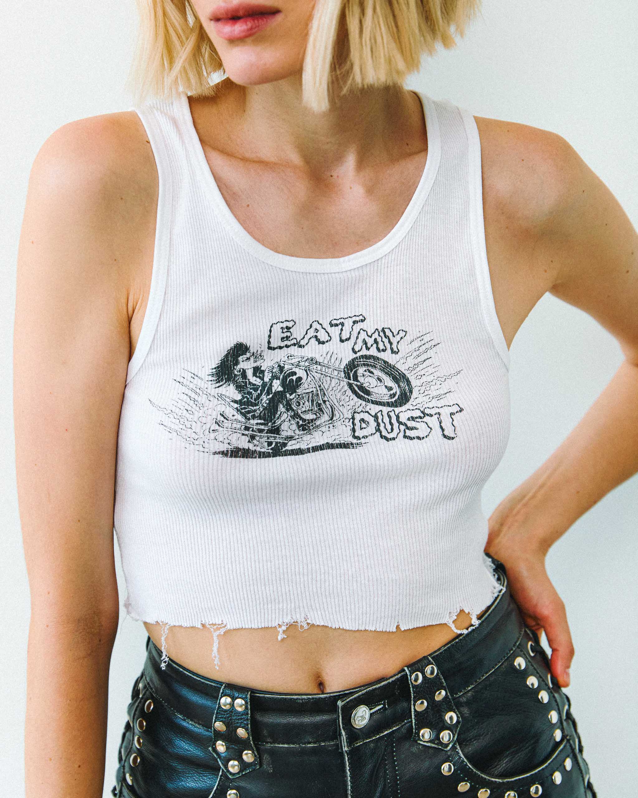 A woman wearing an "Eat My Dust" biker tank top and studded leather shorts.