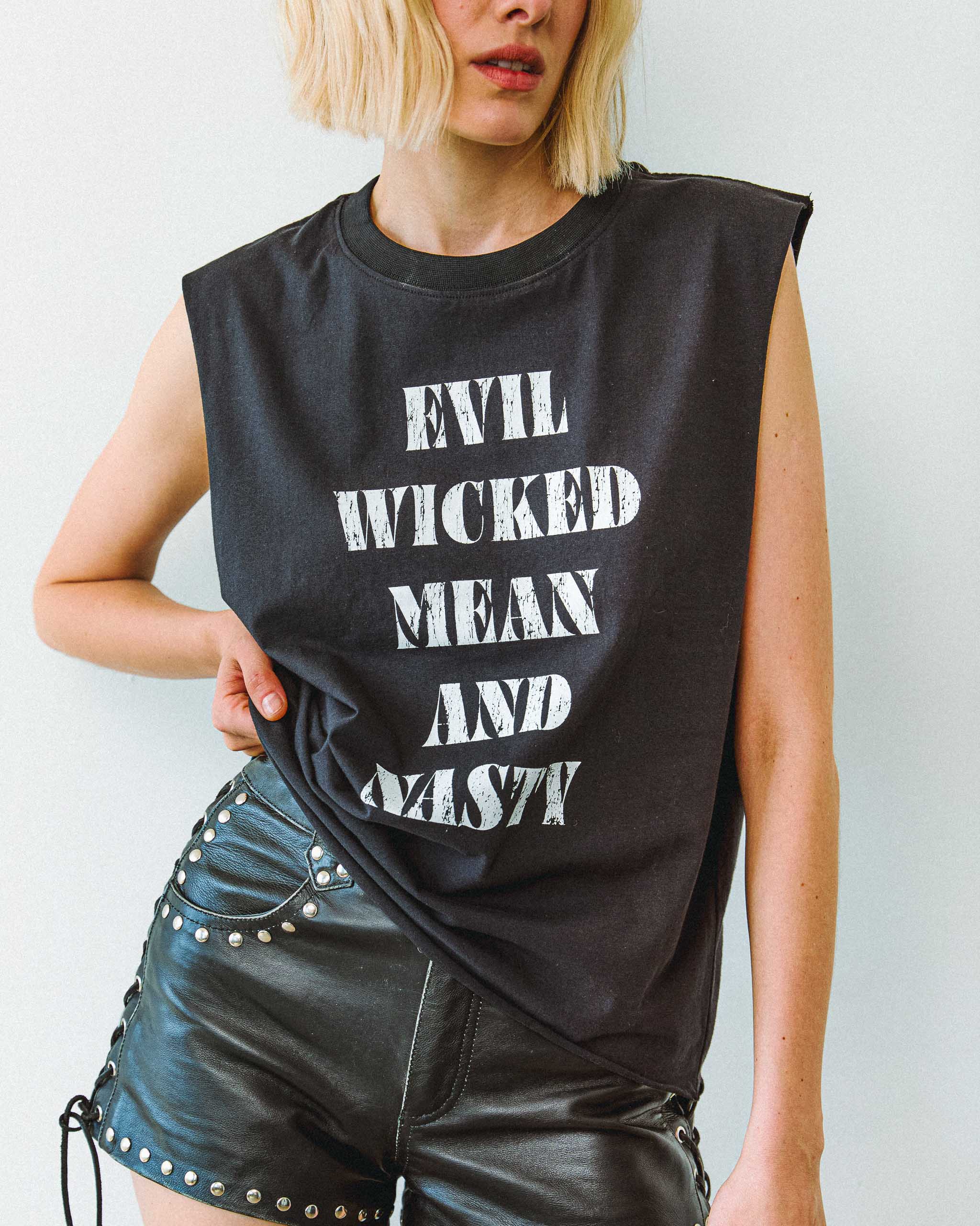 An alt model wearing an "Evil Wicked Mean and Nasty" sleeveless t-shirt and studded leather shorts.