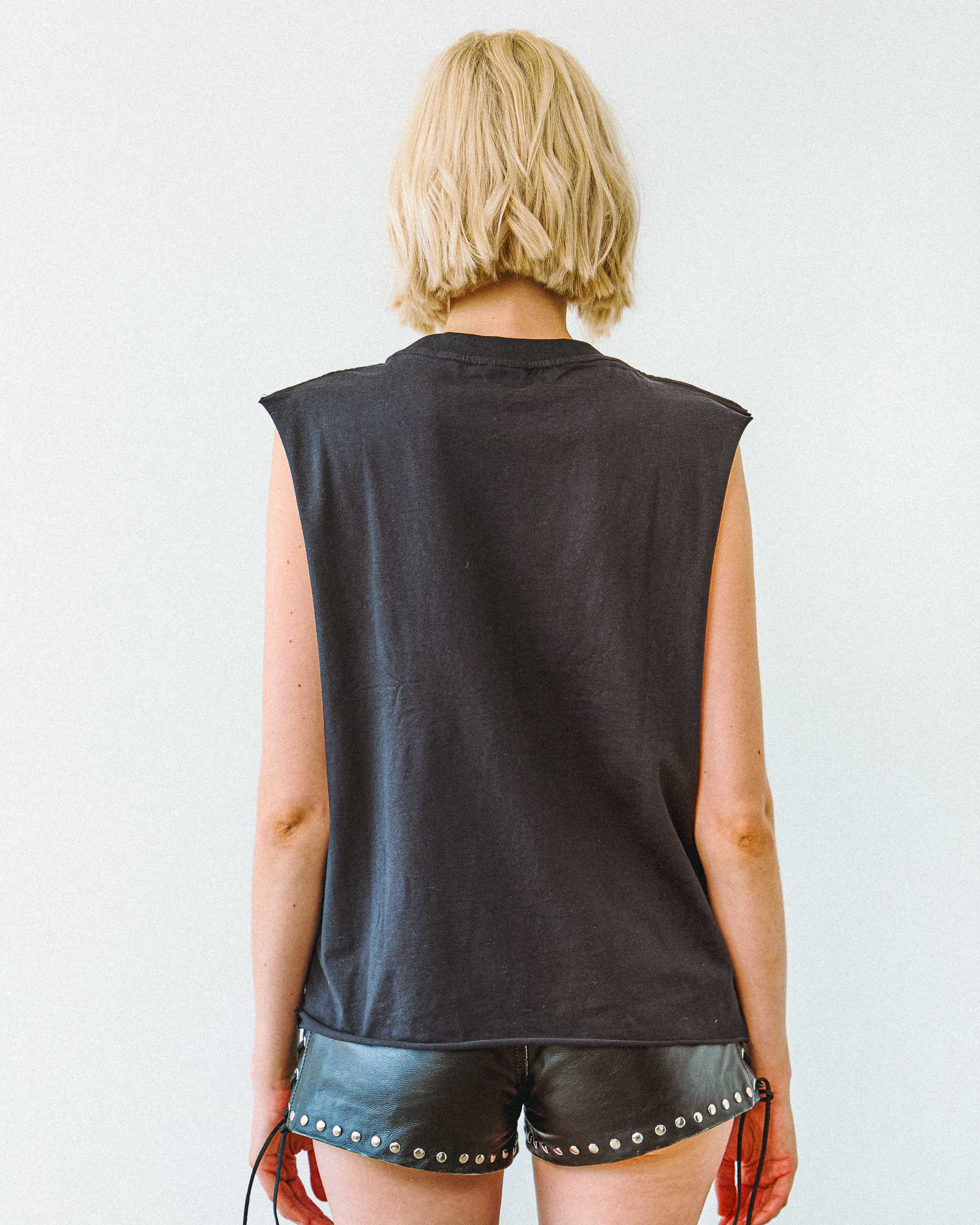 A biker wearing a black sleeveless shirt and studded leather shorts from behind.