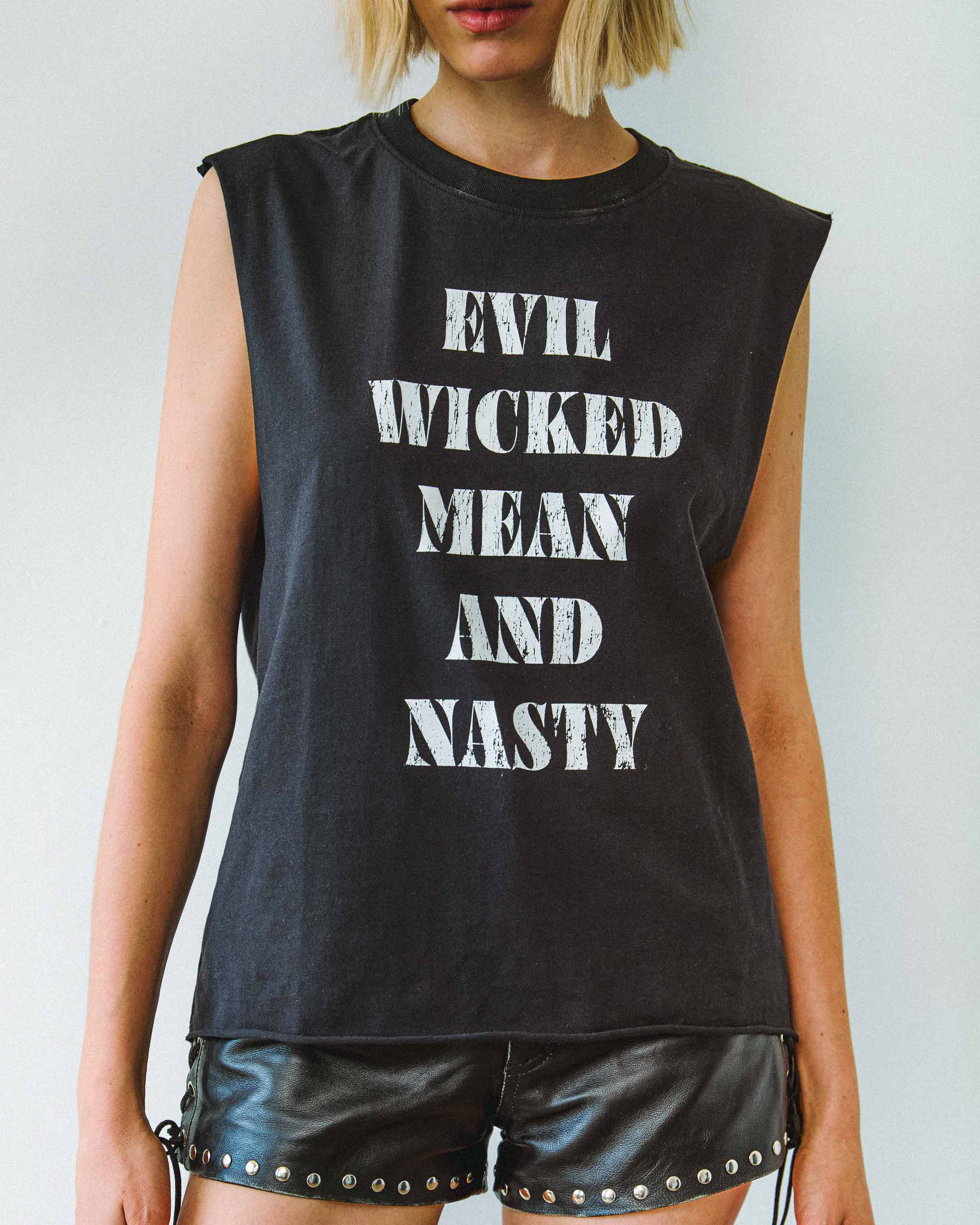 A biker model wearing an "Evil Wicked Mean And Nasty" sleeveless t-shirt and studded leather shorts.