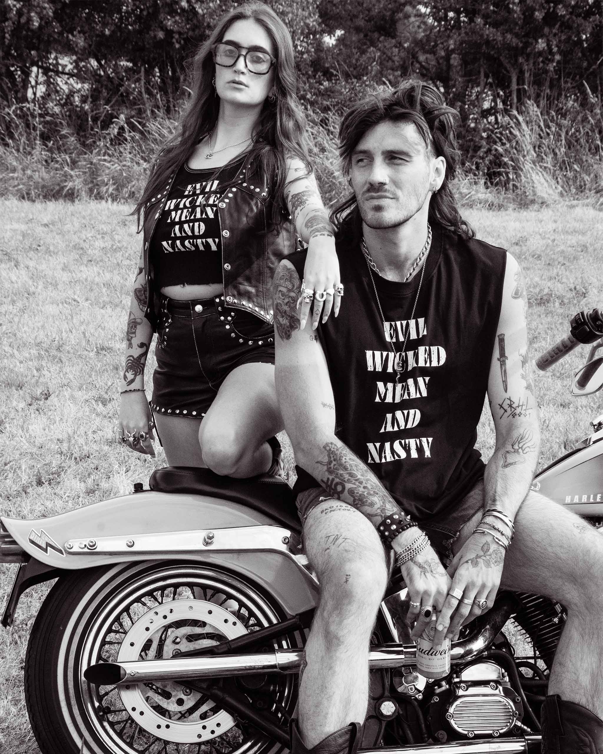 A biker couple wearing matching "Evil Wicked and Nasty" tank tops sitting on a Harley Davidson bike.