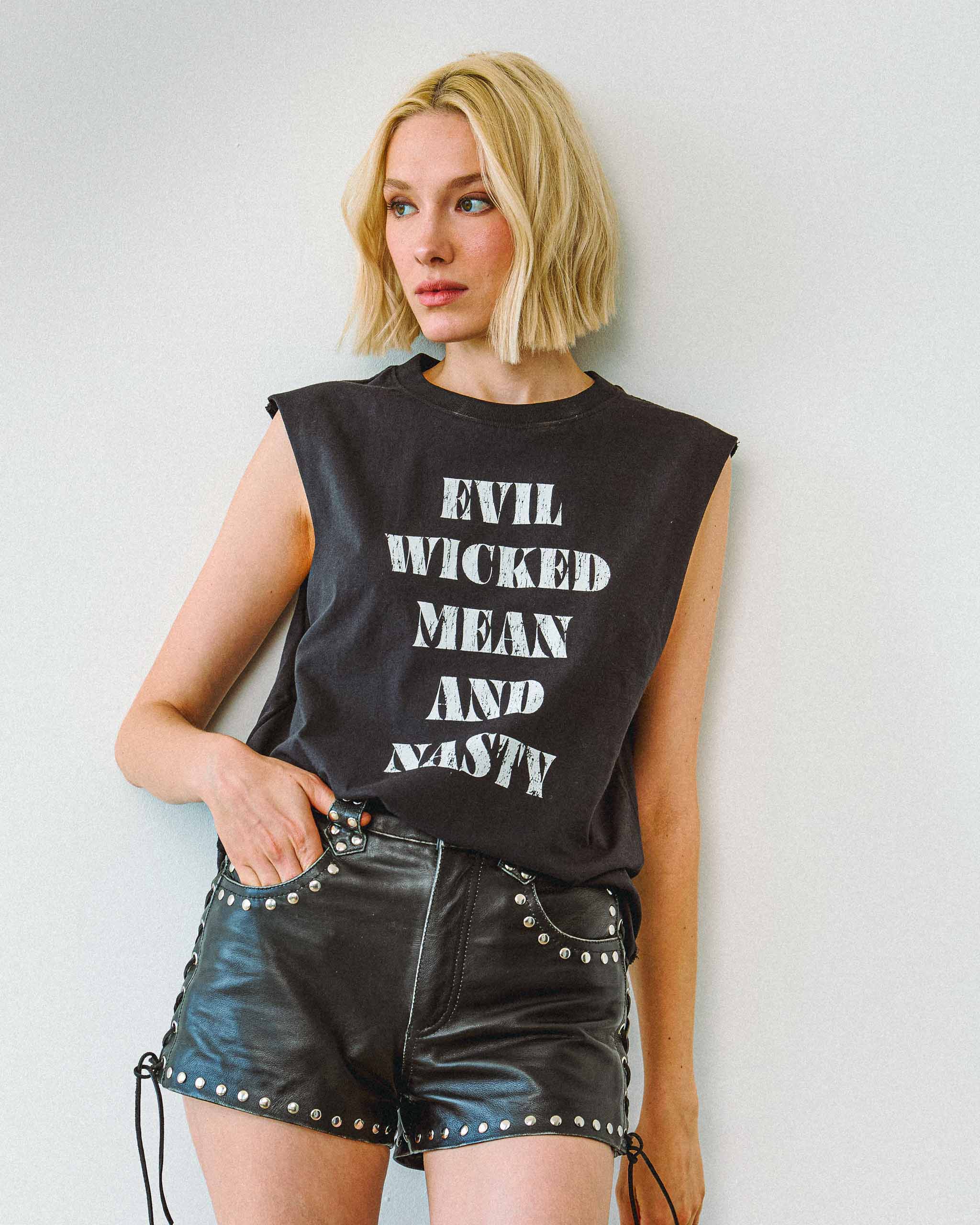 A woman biker wearing an "Evil Wicked Mean And Nasty" sleeveless t-shirt and studded leather shorts.