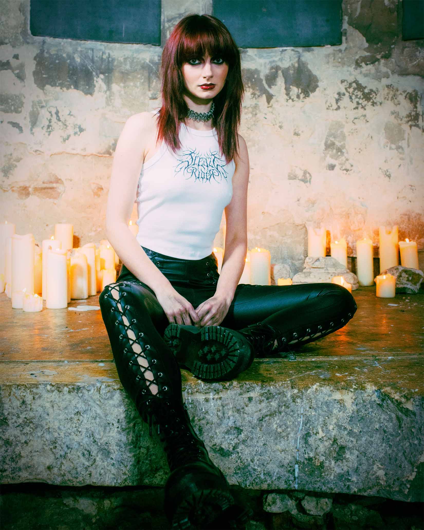 A goth sitting amongst candles in an old church