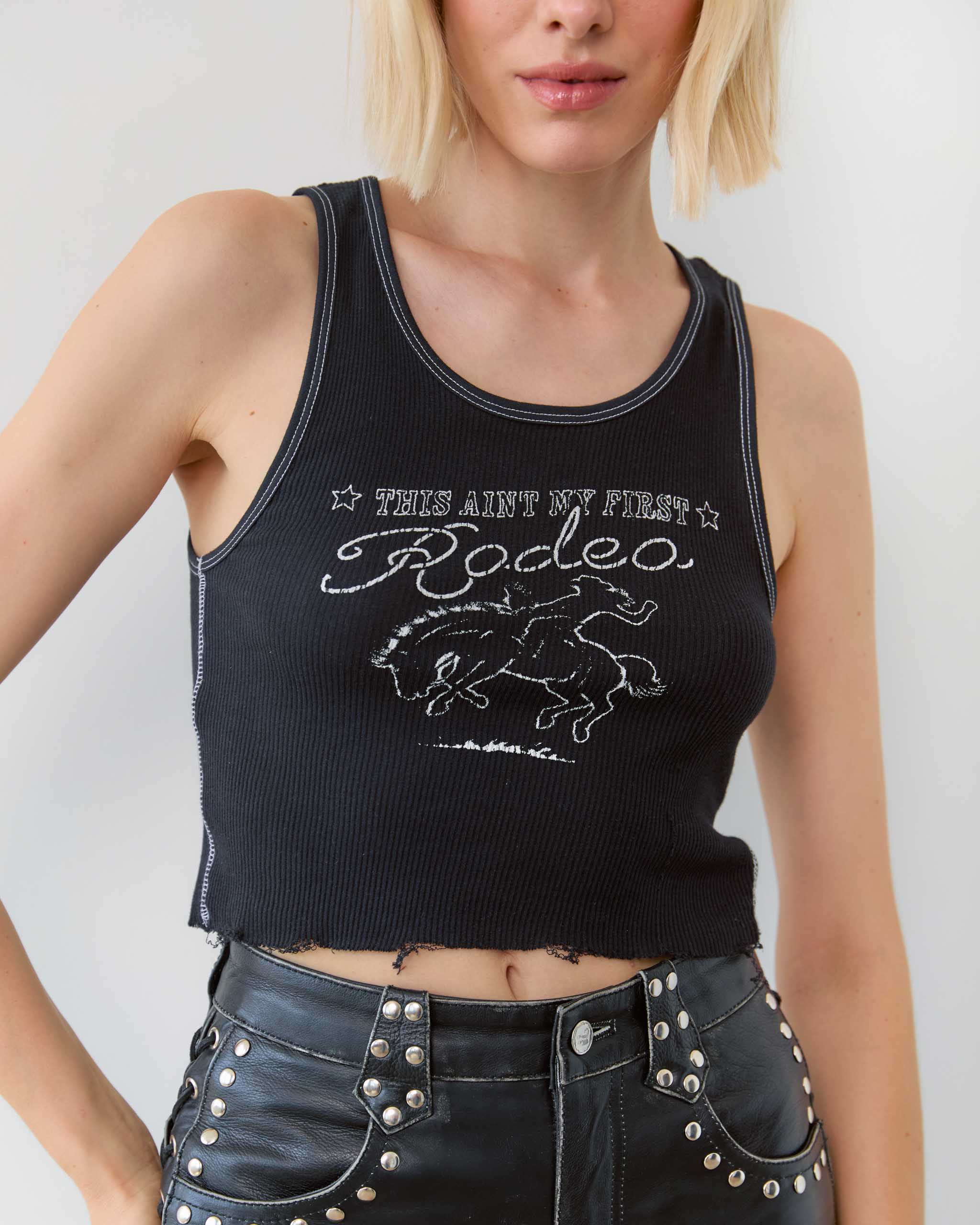 Black tank top with 'This Ain't My First Rodeo' text and rodeo horse graphic worn by a cowgirl.