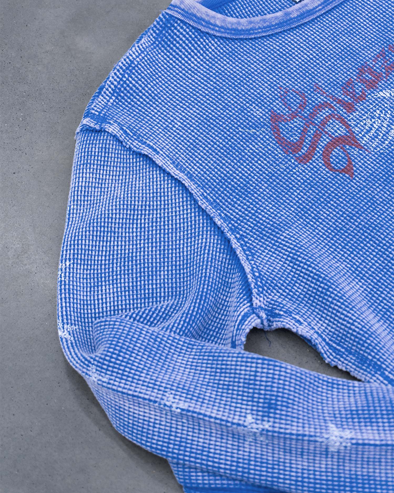 A close-up of a blue waffle knit long sleeve top with a heavy faded wash, swooping eagle screen print and stars up the sleeves.