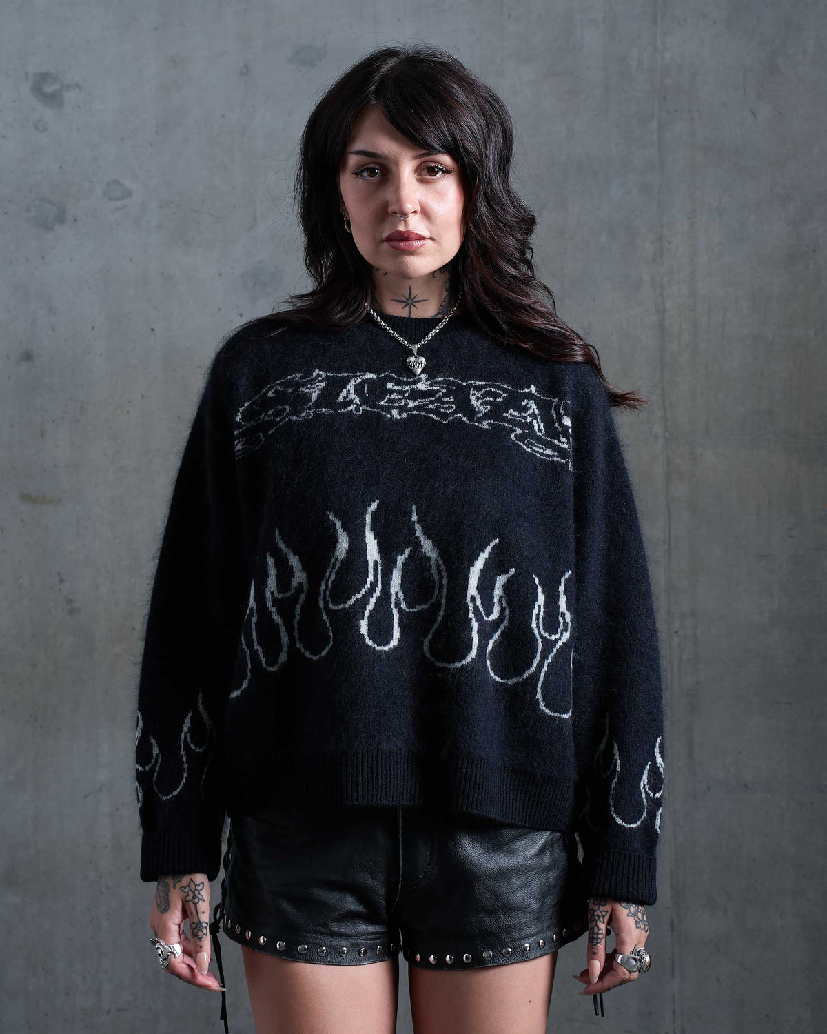 An alt model with tattoos wearing a gothic black knitted sweater with white flames, and studded leather shorts.