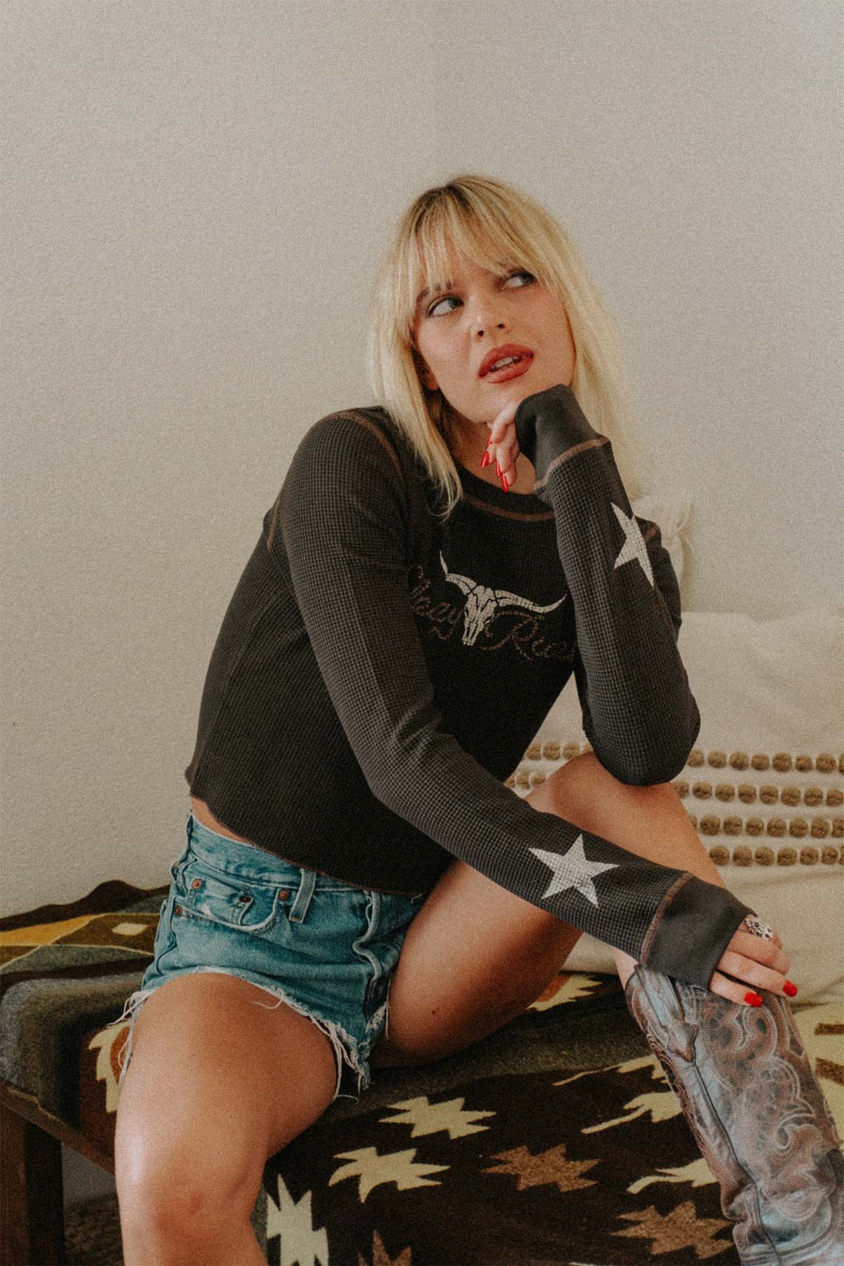 A woman sitting on a western rug, wearing a waffle knit with a cow skull on the front and stats on the sleeves.