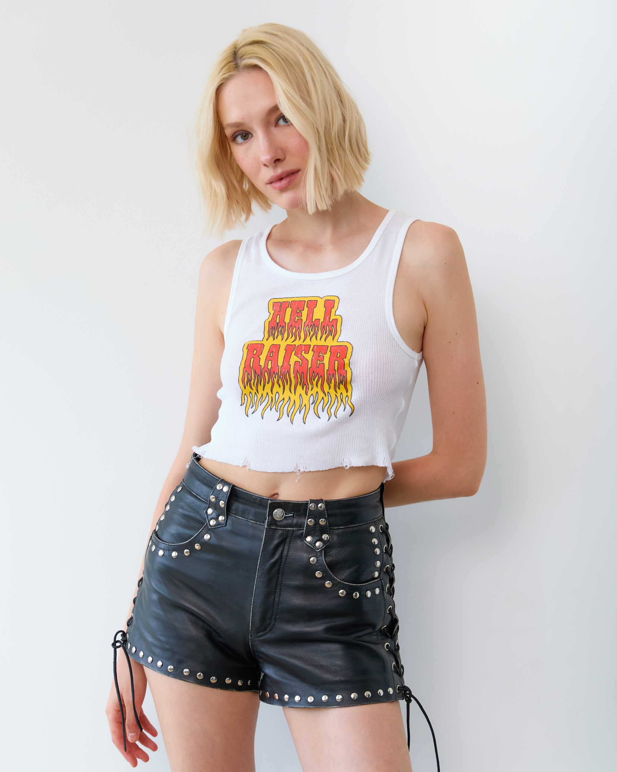 A woman wearing a tank top with flaming Hell Raiser text, and biker leather shorts.