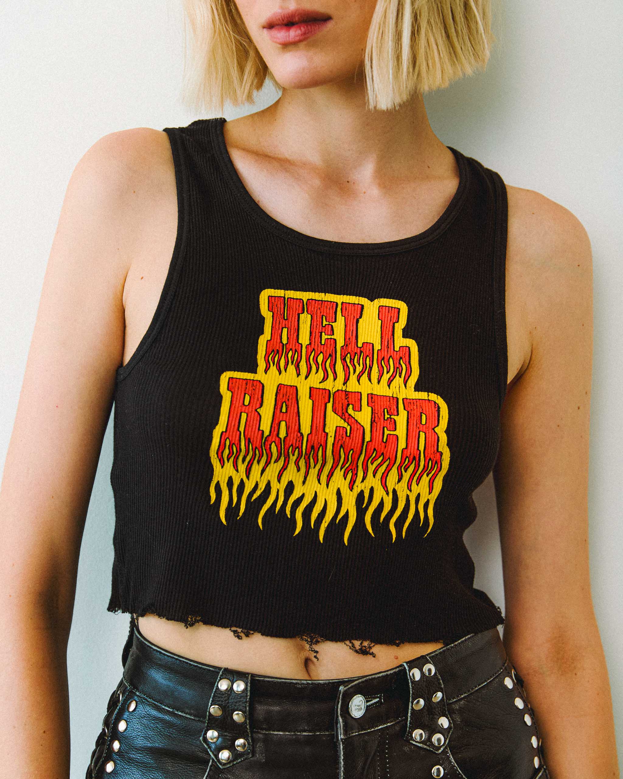 Woman wearing a black Sleazy Rider "Hell Raiser" rock and roll tank top and studded leather shorts on a plain background.