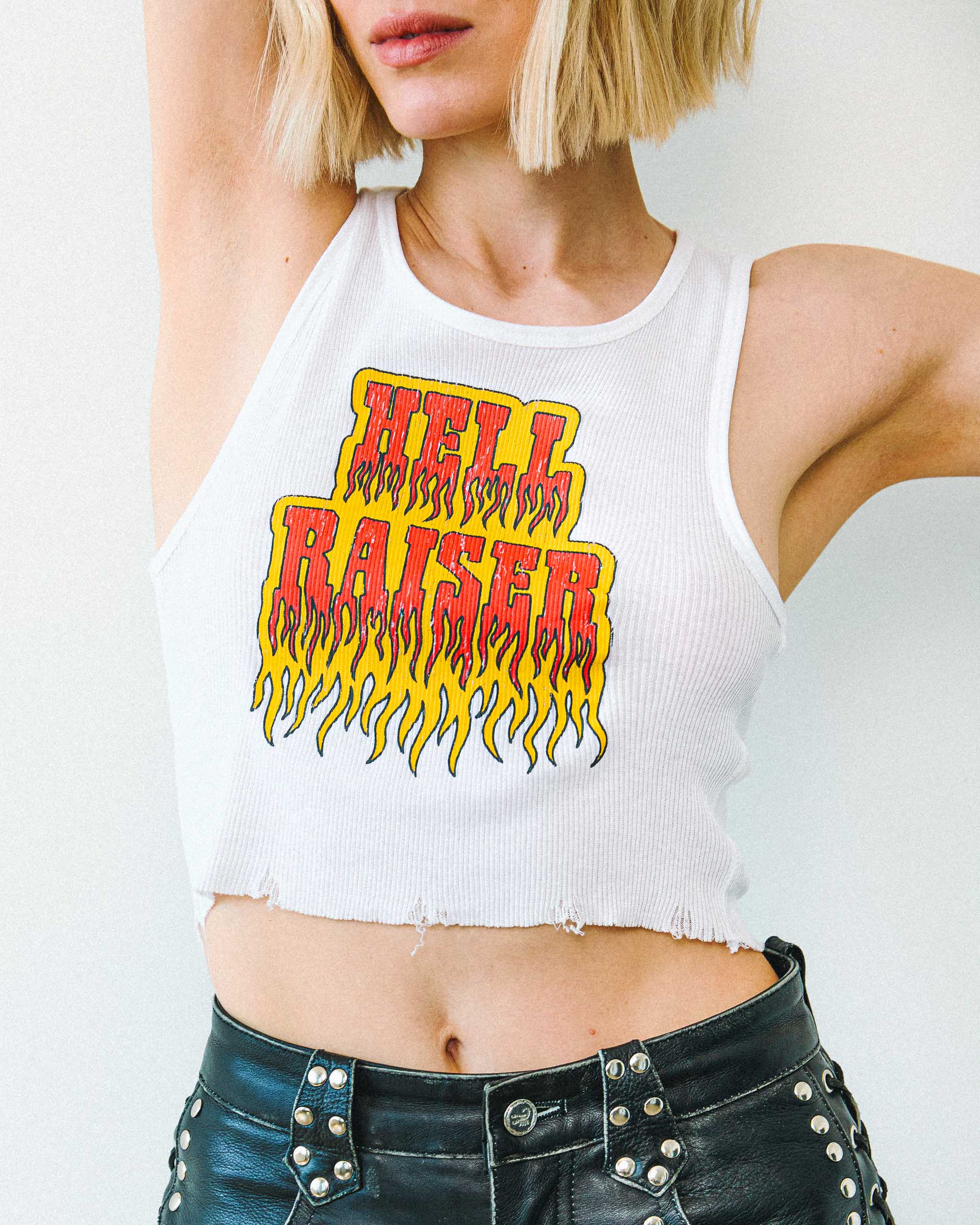 Woman wearing a Sleazy Rider "Hell Raiser" gothic tank top and studded leather shorts, on a plain background.