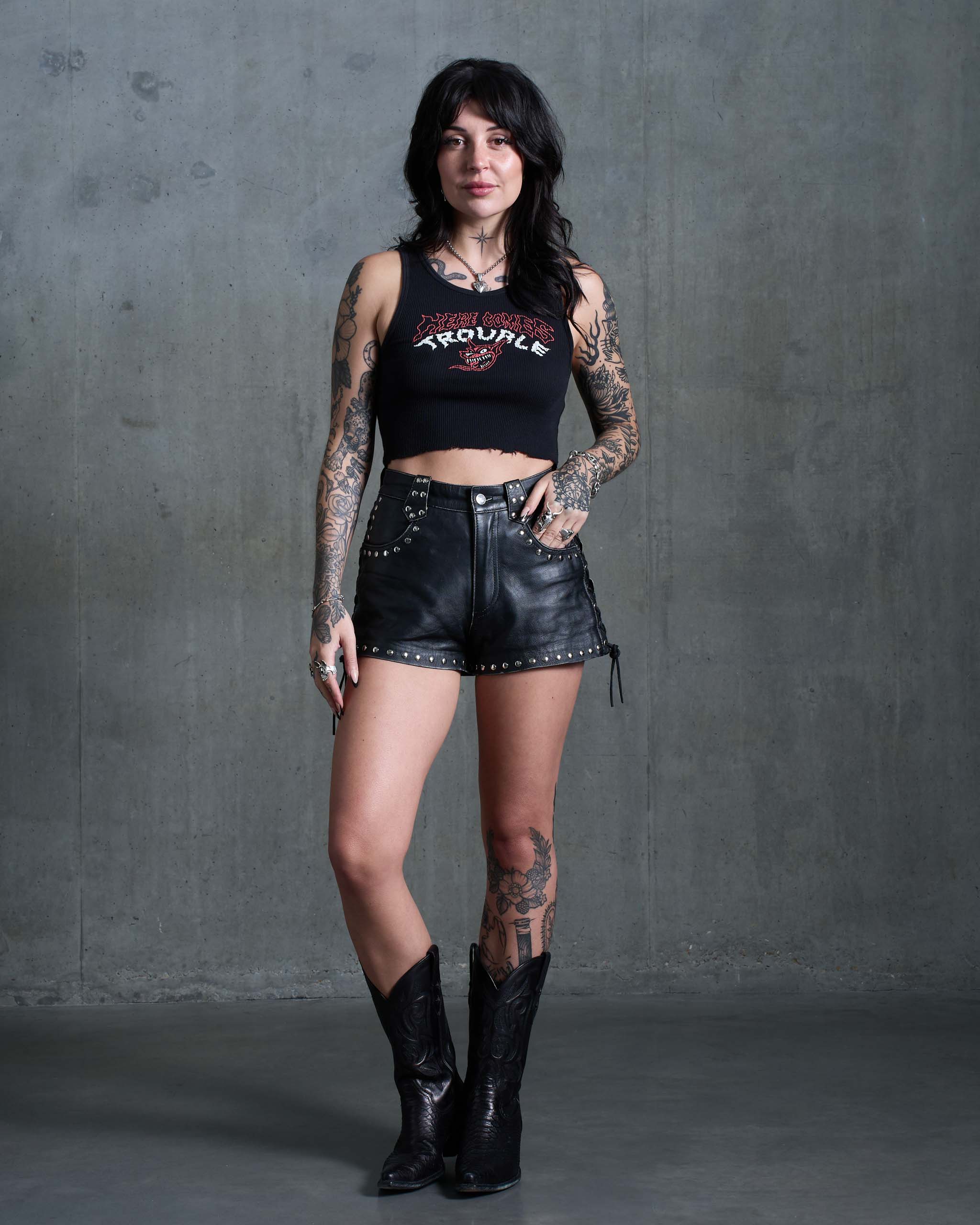 A rock and roll woman wearing a punk tank top, studded leather shorts and cowboy boots.