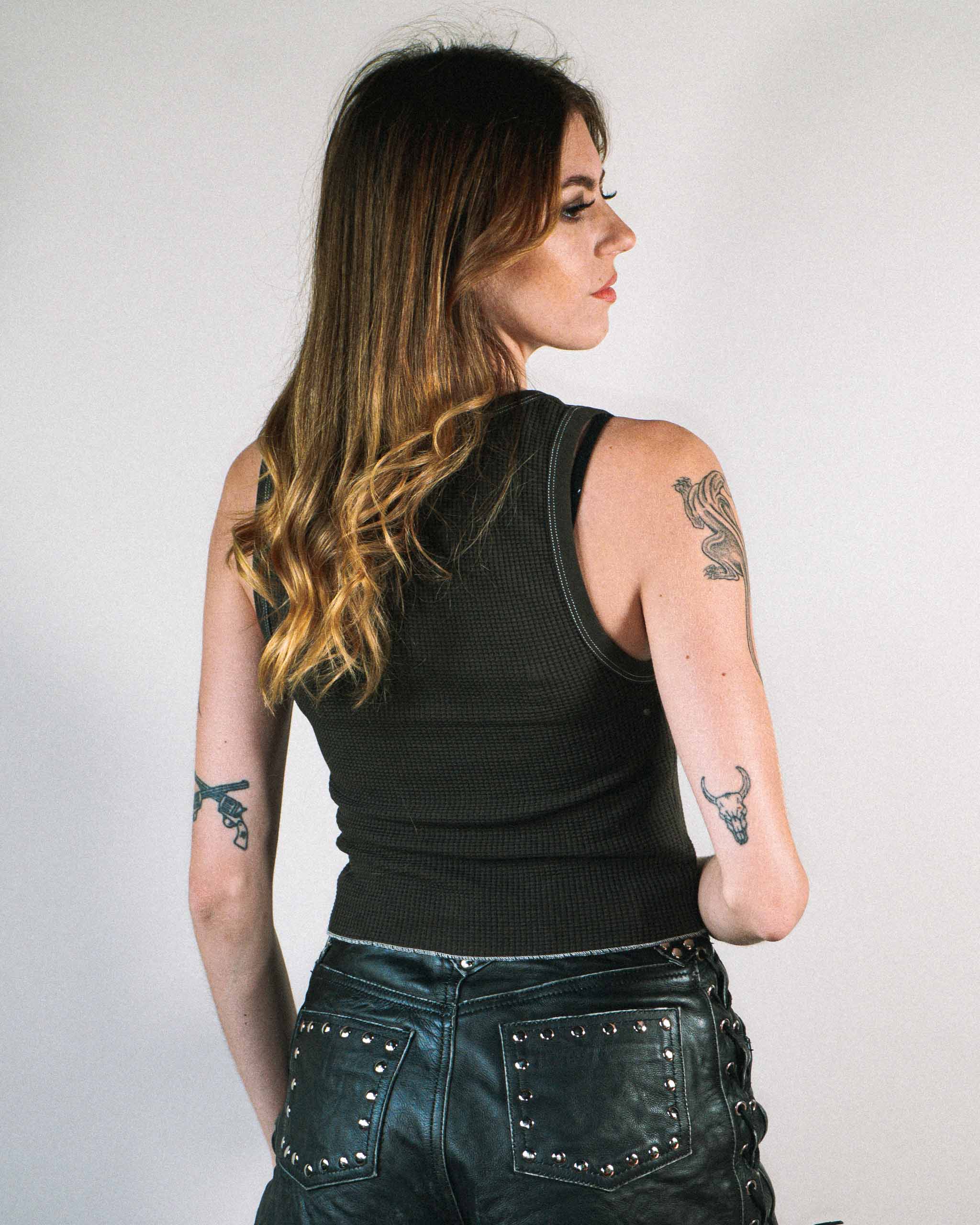 Back view of an alt woman wearing a dark western tank top and studded leather shorts.