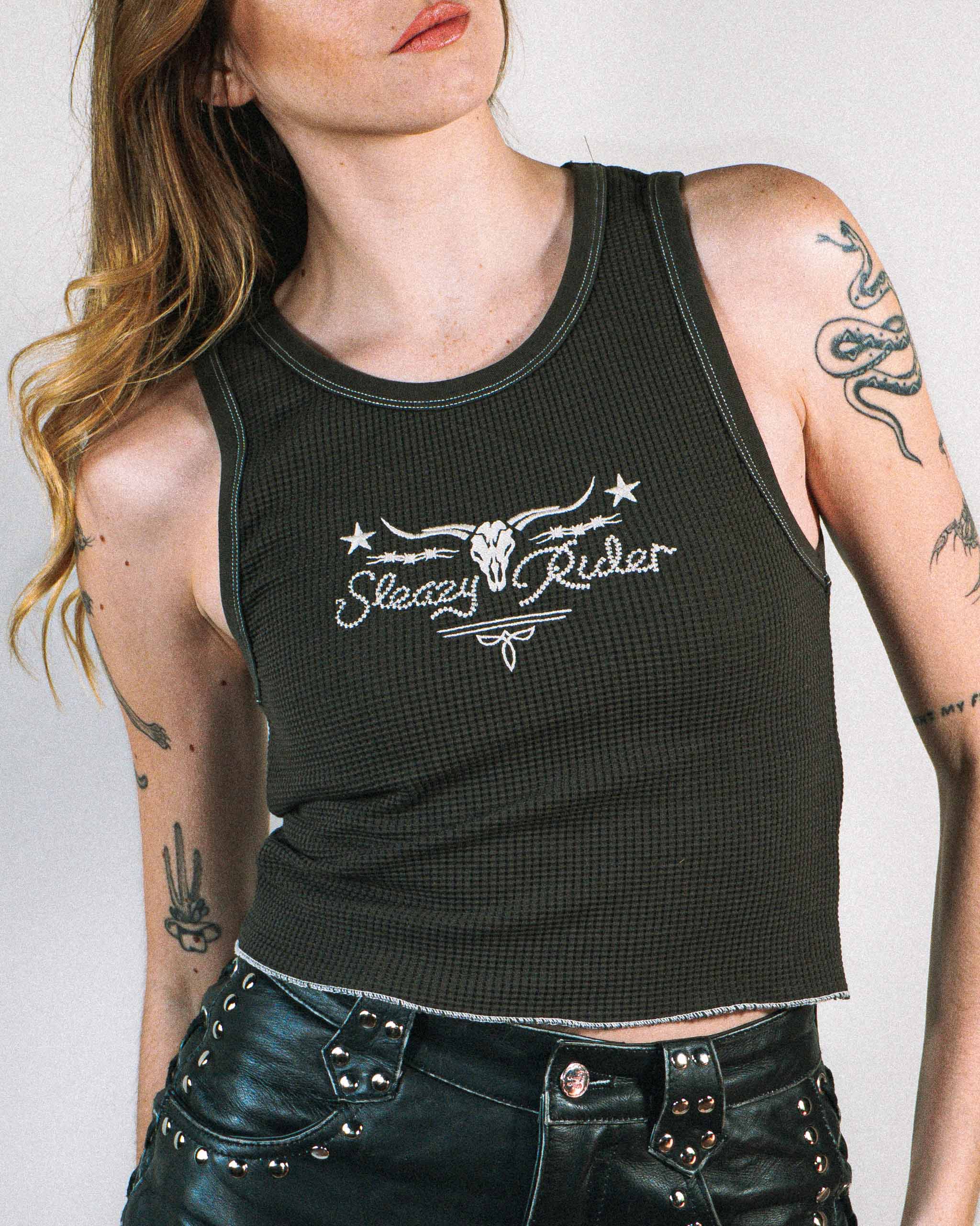 Alt model wearing a dark western tank top with cow skull embroidery and studded leather shorts.
