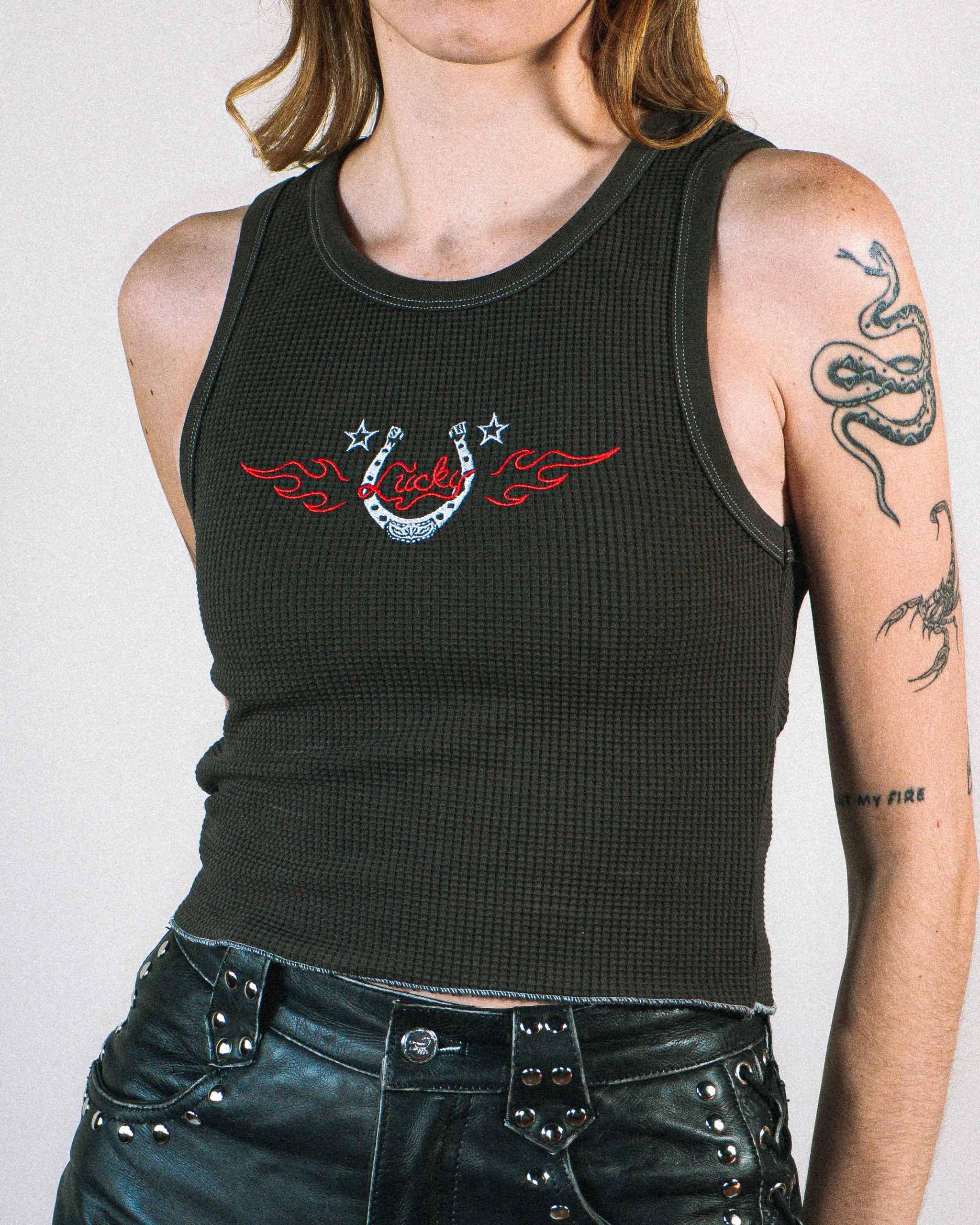 Woman wearing a dark western tank top with a flaming horseshoe embroidery.