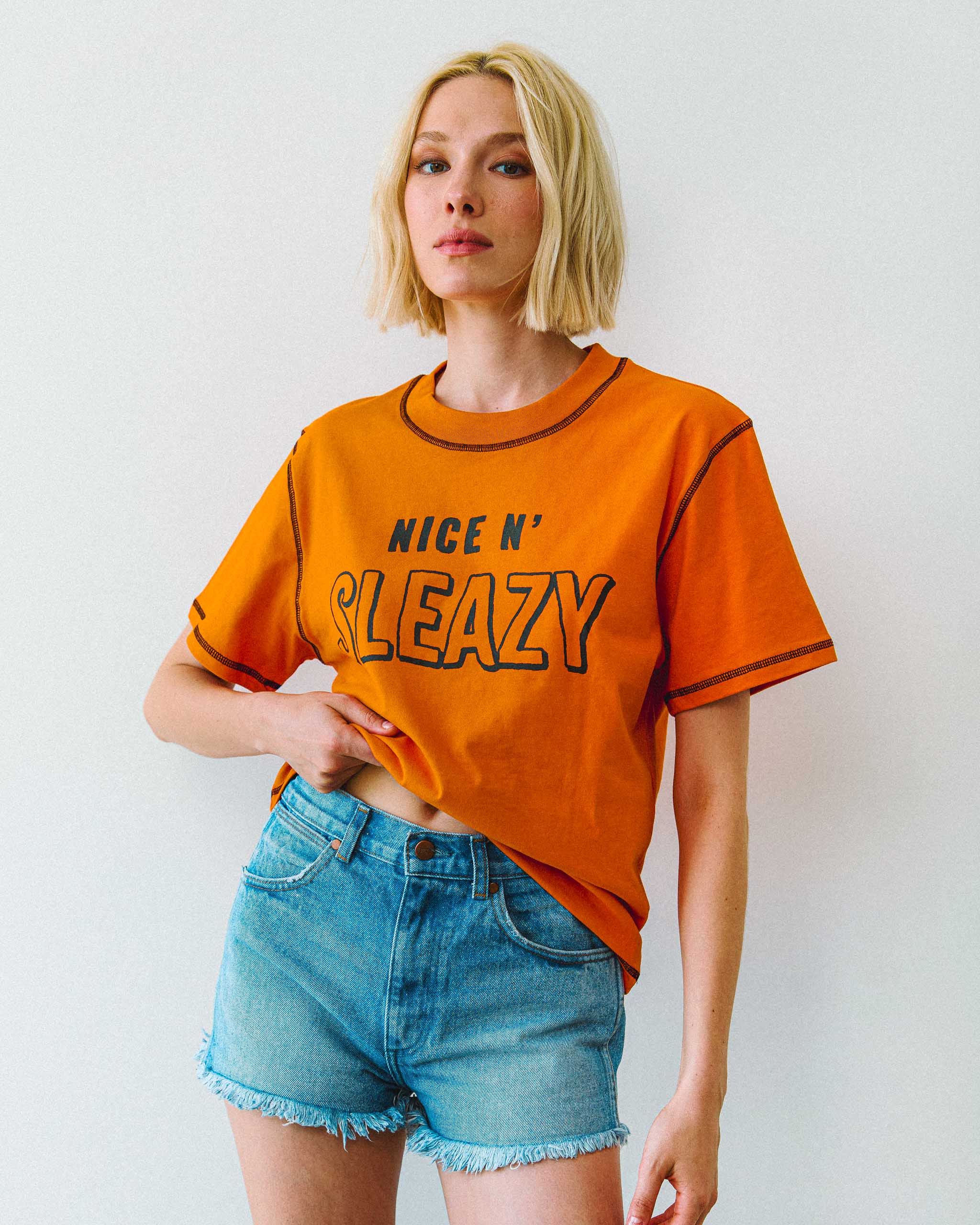 A young model wearing an orange biker t-shirt with "NICE N' SLEAZY" slogan on the font.