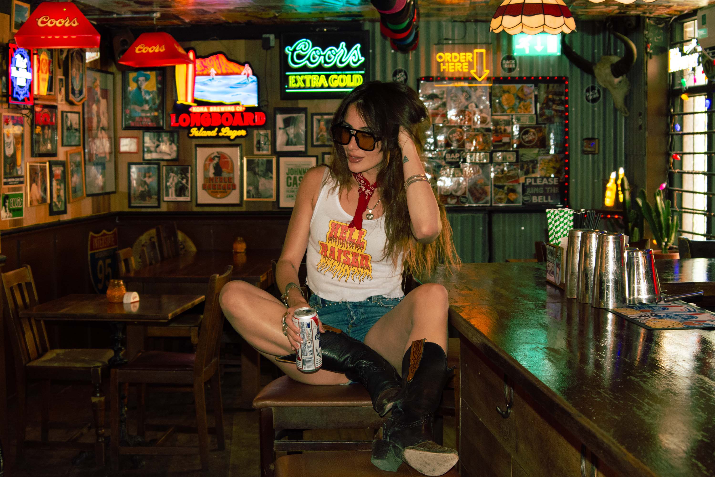 A woman sat in a country bar, with neon signs around.