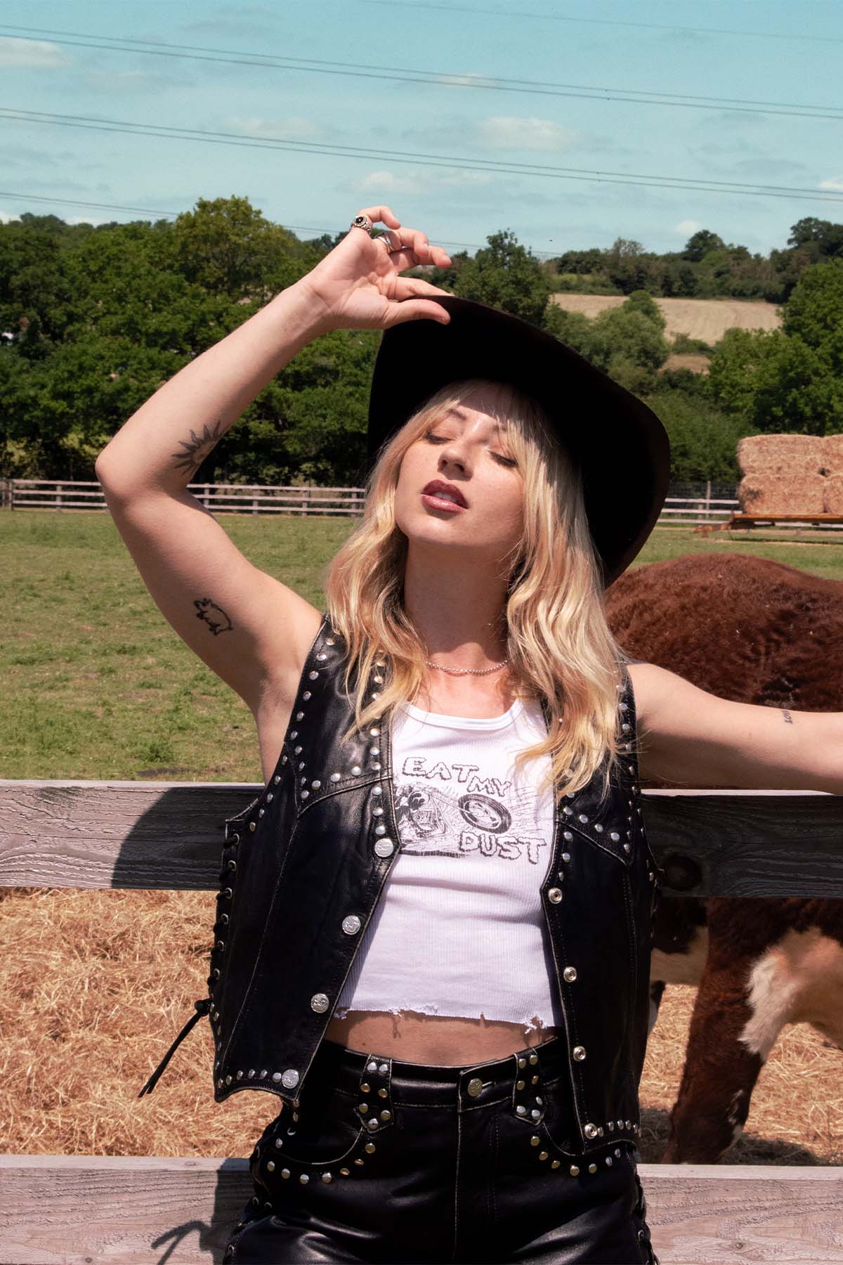 Person wearing a black studded leather jacket and white graphic t-shirt in an outdoor setting on a ranch