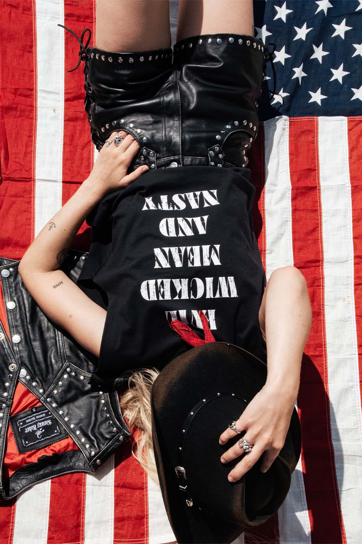 A gothic cowgirl wearing a black t-shirt with white text on an American flag background