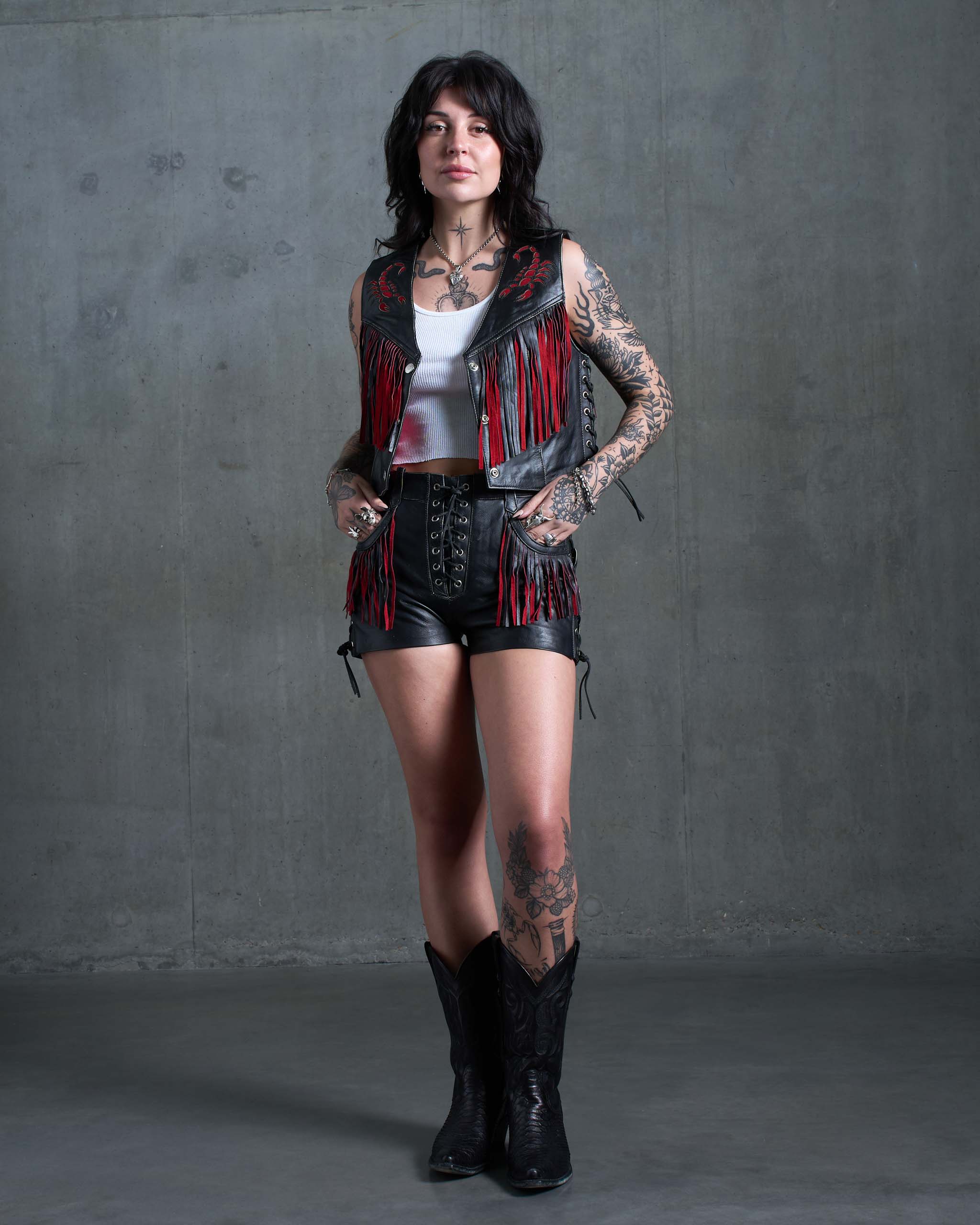 A tattooed model wearing a biker vest and shorts with red suede scorpion details.