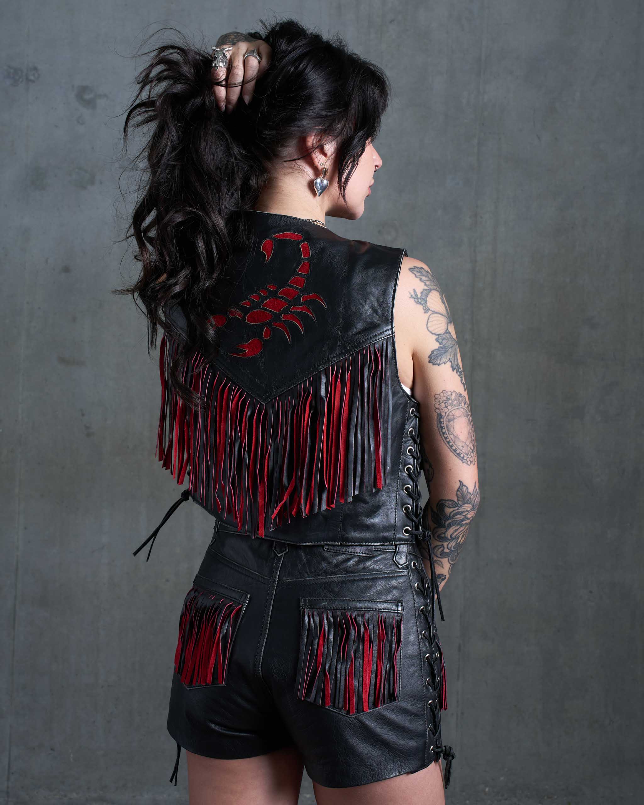 A tattooed model showing the back of a black leather biker vest with red suede scorpion detail.