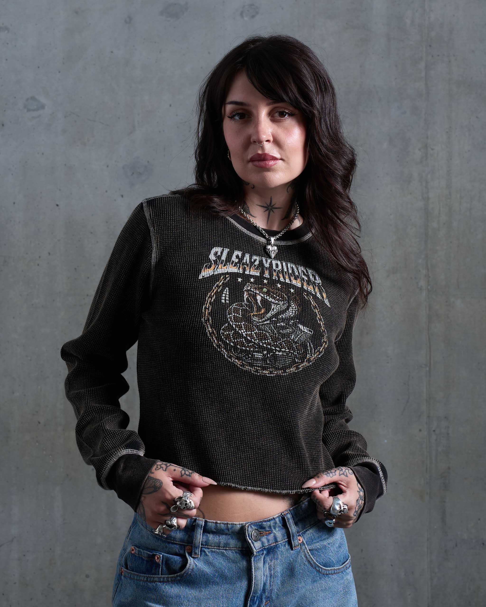 A biker woman wearing a vintage faded waffle knit top with a rattlesnake print, and low rise jeans.