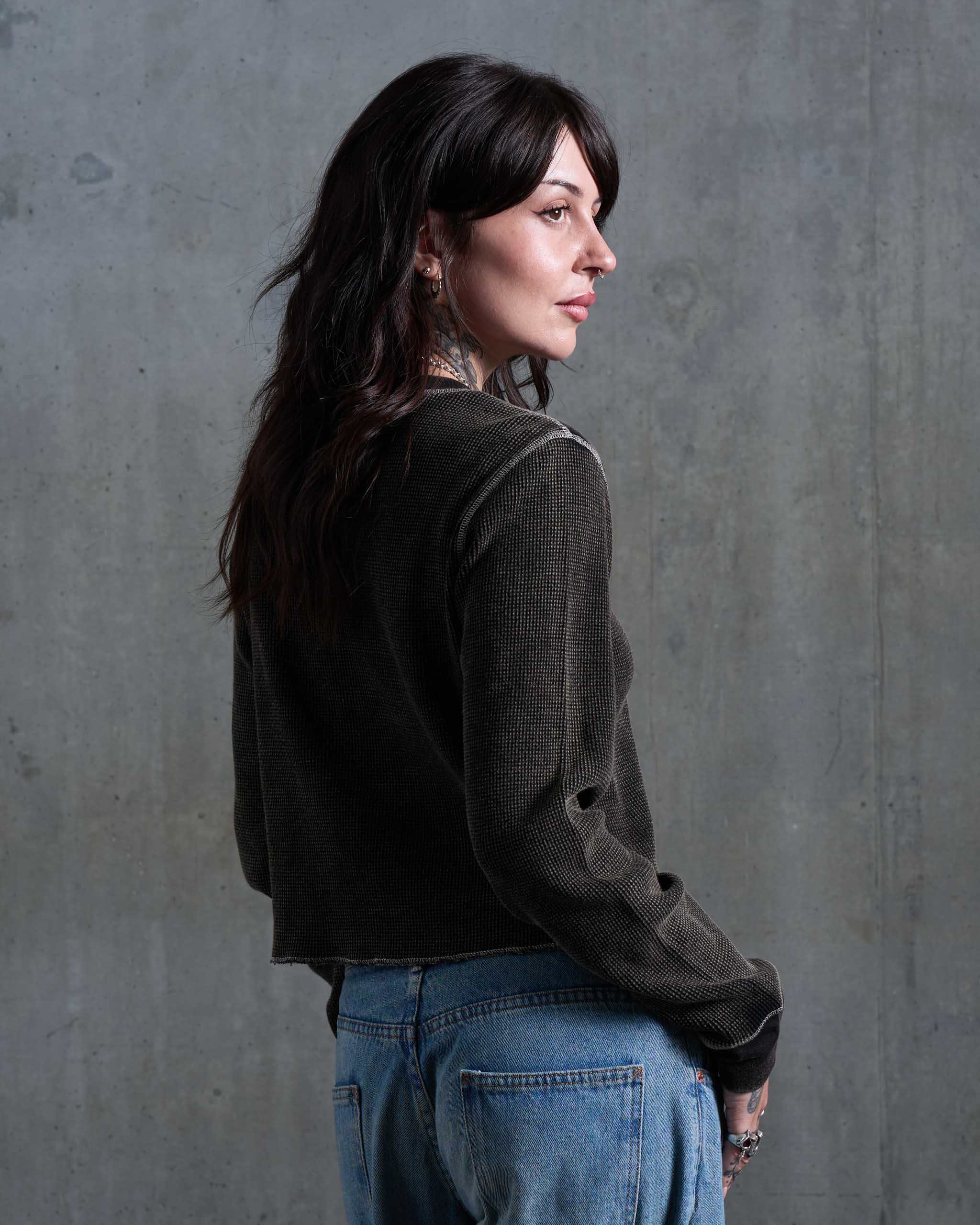 A tattooed woman wearing a vintage faded waffle knit top, with low rise jeans, viewed from behind.