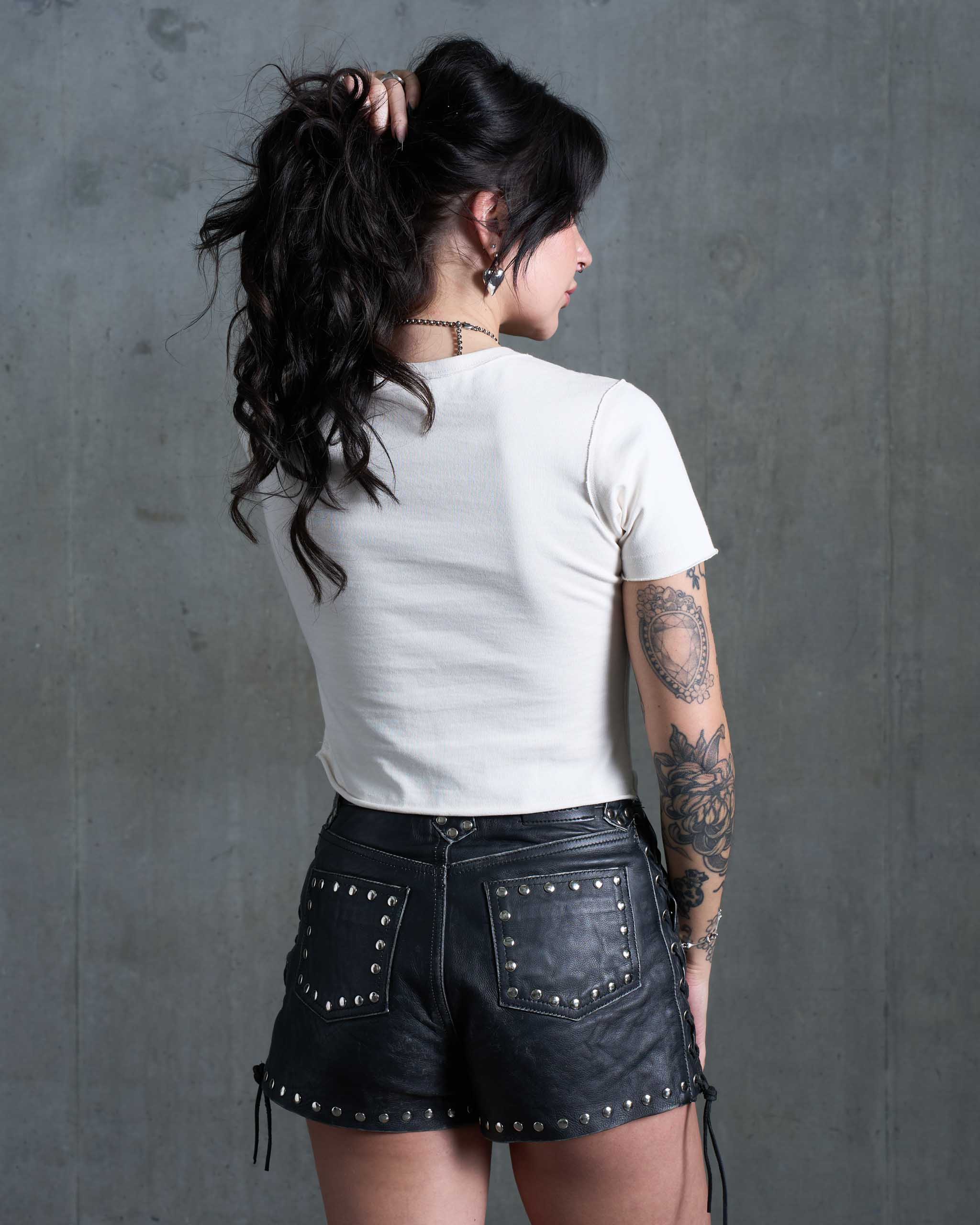 A woman wearing an off white baby tee and studded leather shorts.