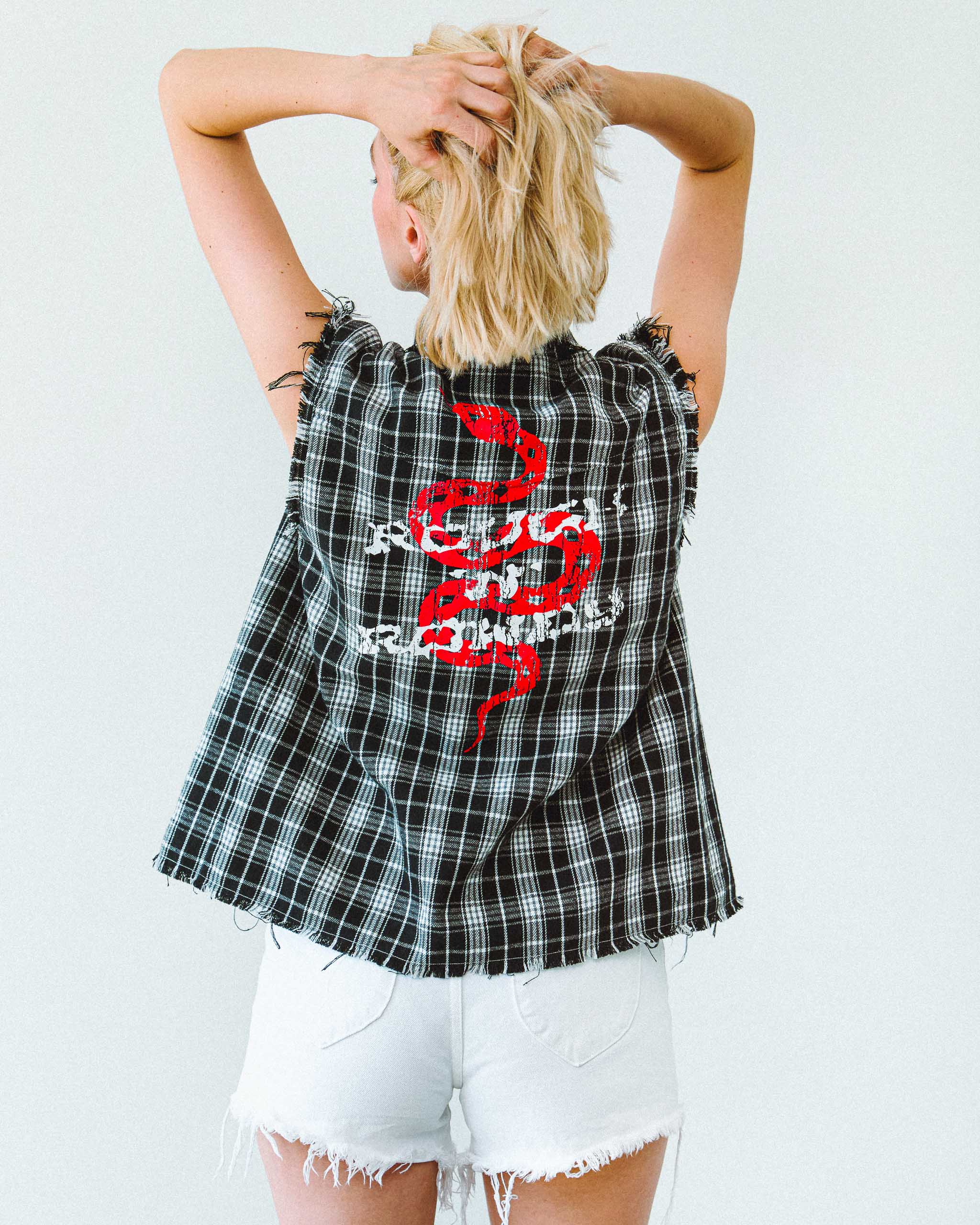 A model wearing a black and white flannel cut off shirt, with a snake print on the back.
