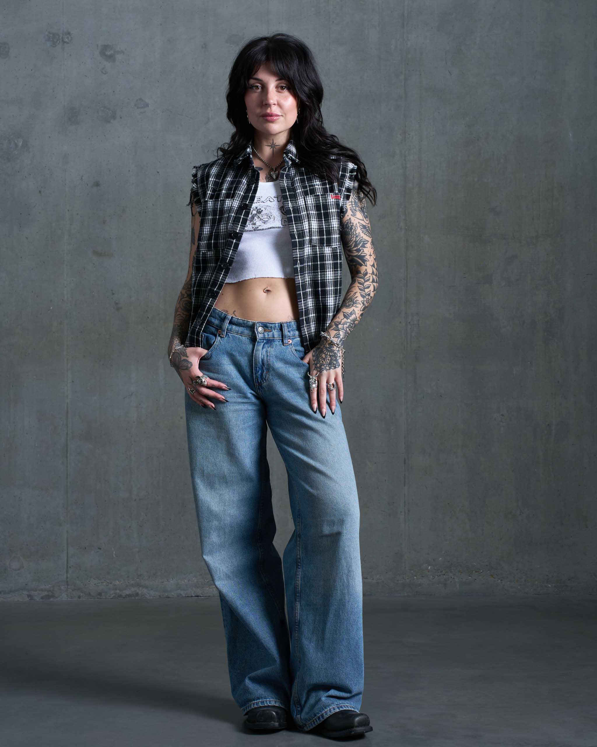 A tattooed woman wearing a flannel cut off and jeans.