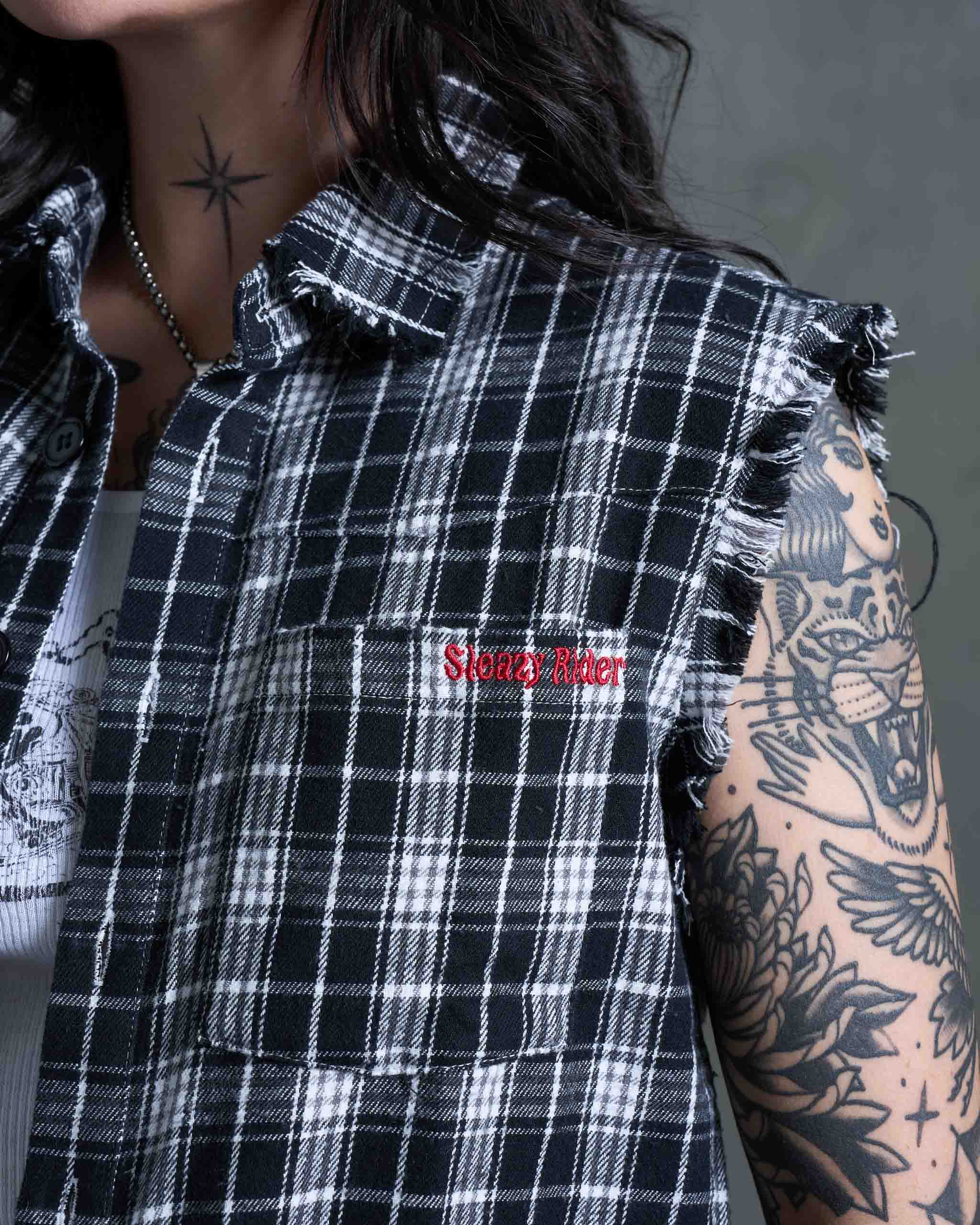 A tattooed woman wearing a flannel cut off with Sleazy Rider embroidery.