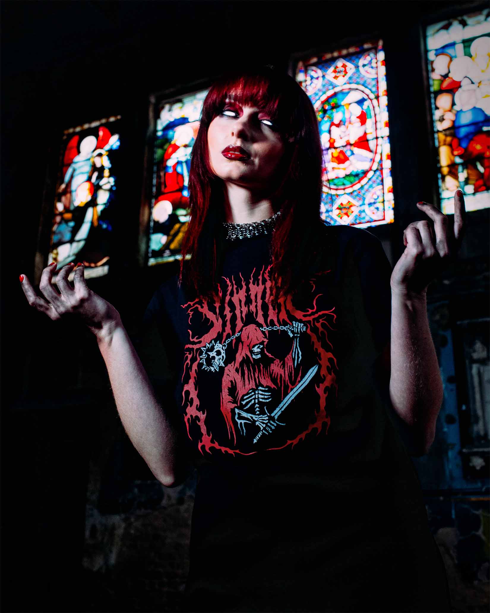 A gothic girl wearing an alternative t-shirt in front of some stained glass church windows