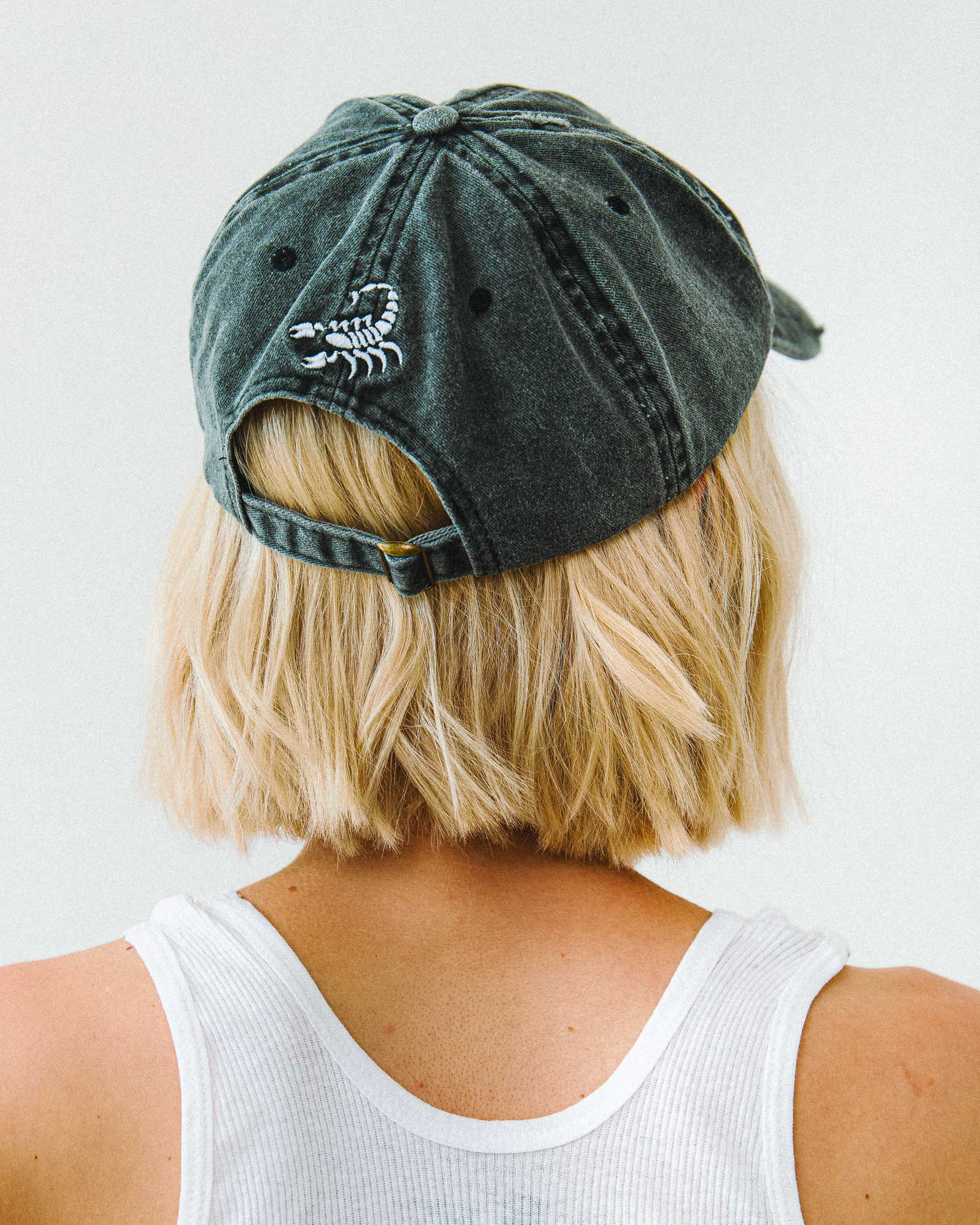 A woman wearing a Sleazy Rider cap with scorpion embroidery on the back.