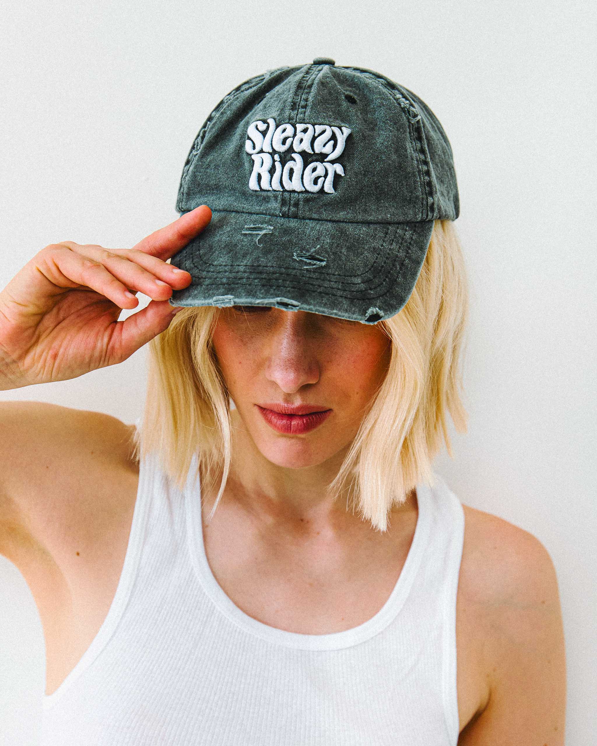 A young woman wearing a Sleazy Rider  acid wash distressed cap.