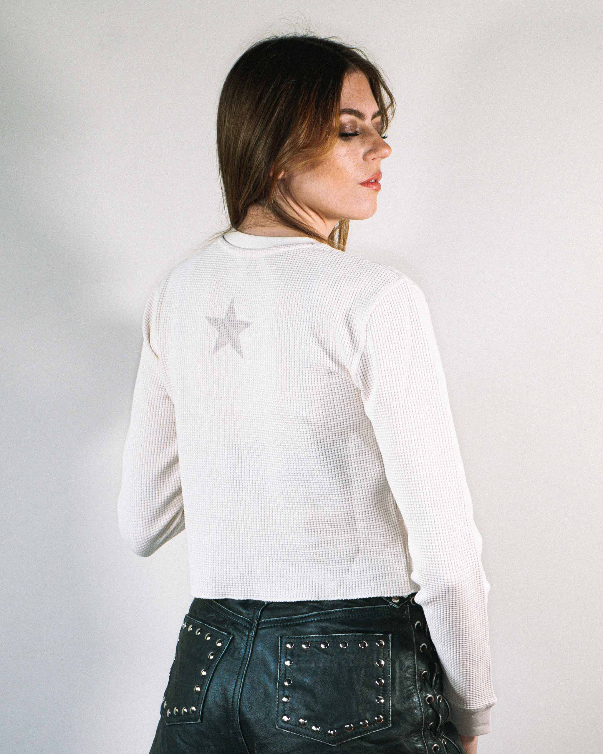Back view of an alt model wearing an off white waffle knit top and leather shorts.