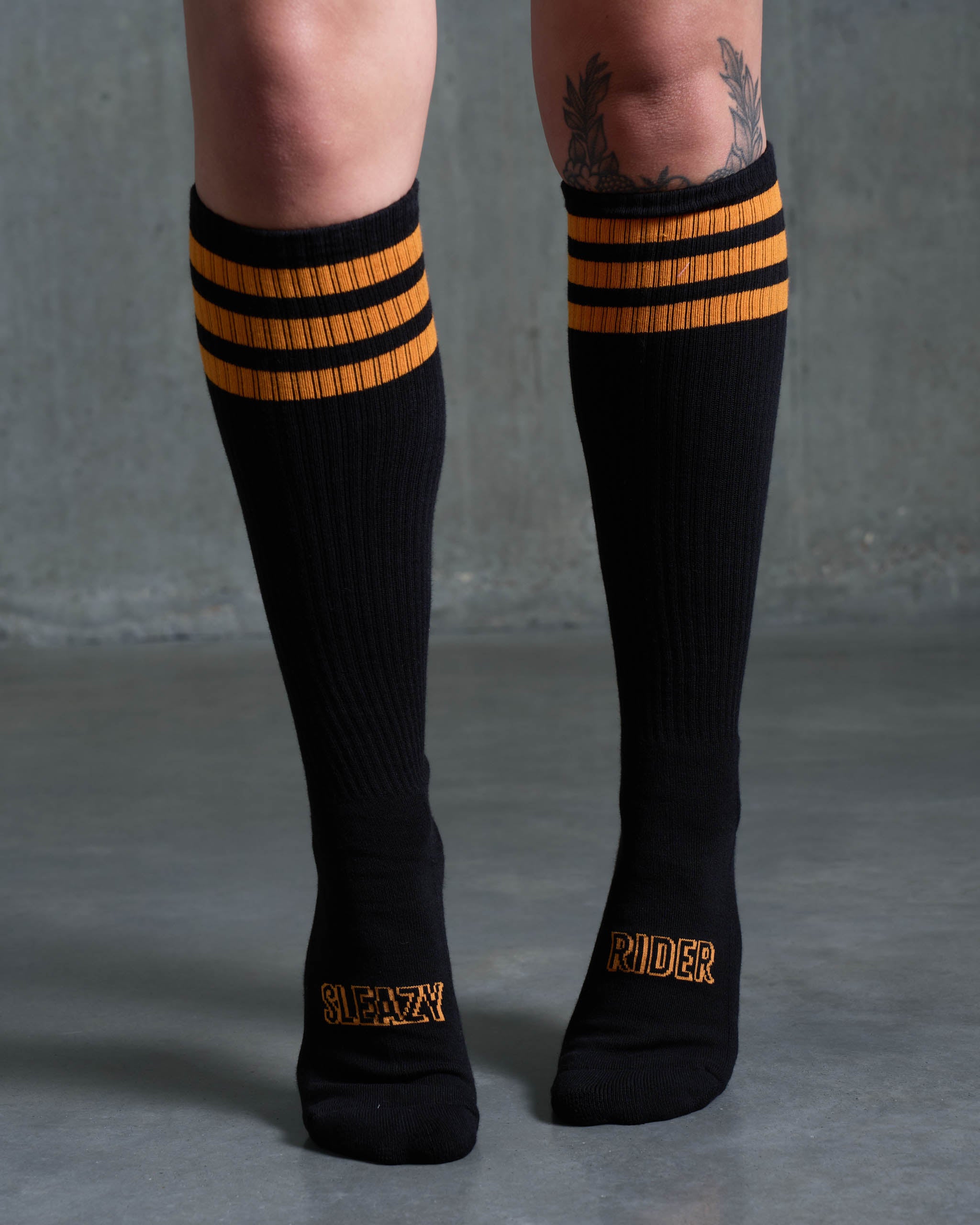 A tattooed woman wearing some Sleazy Rider black and orange socks.