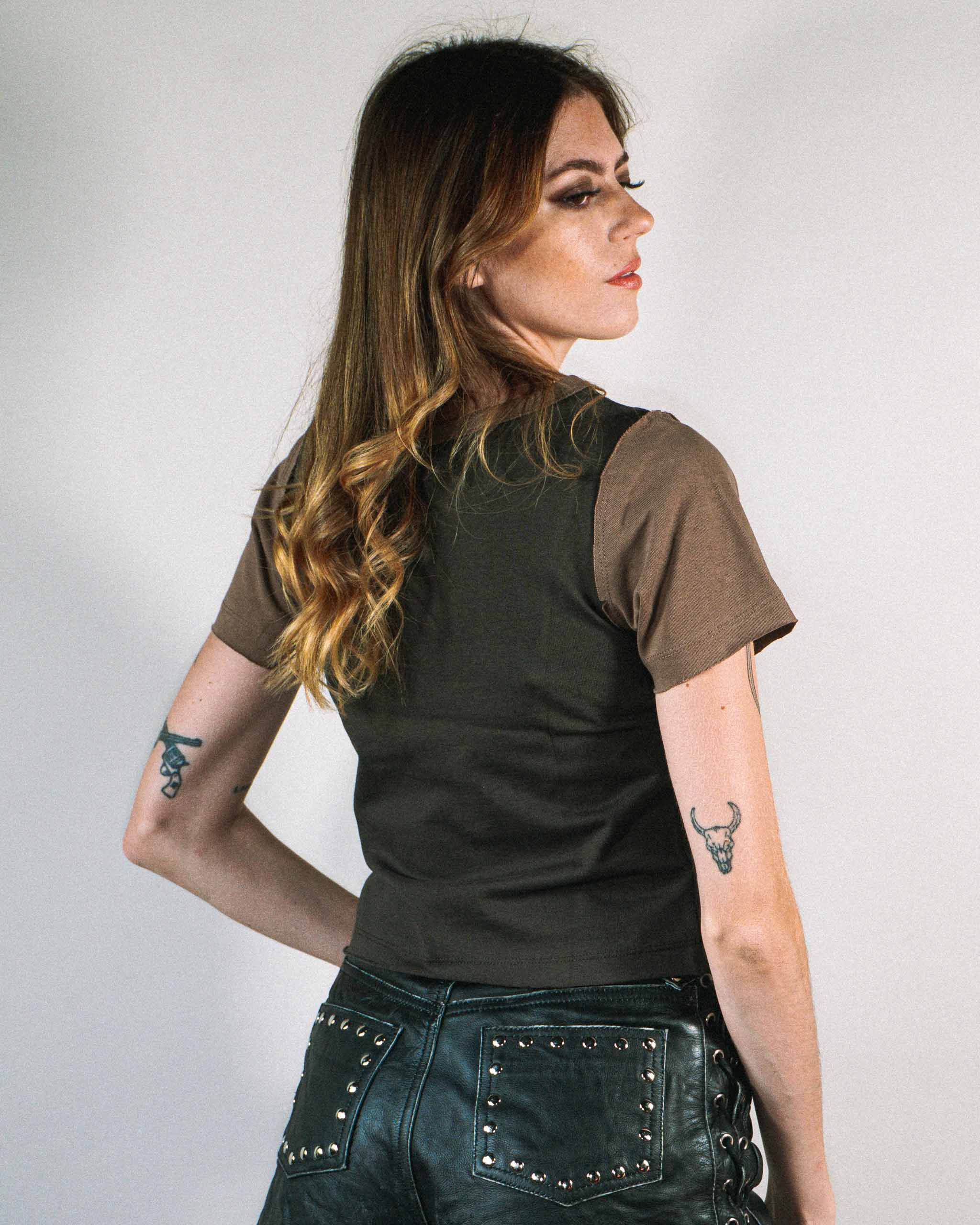 The back view of a woman wearing a dark western baby t-shirt with brown sleeves and studded leather shorts