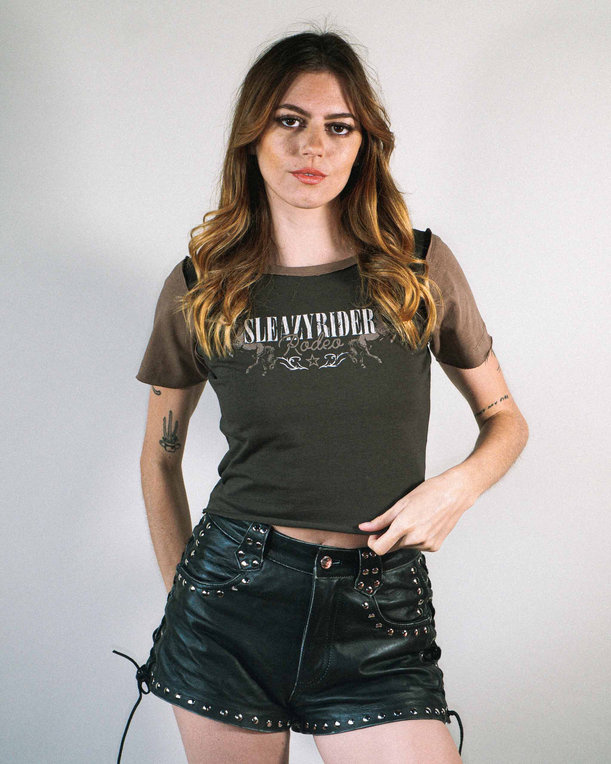 A woman wearing a dark western baby t-shirt with brown sleeves and studded leather shorts