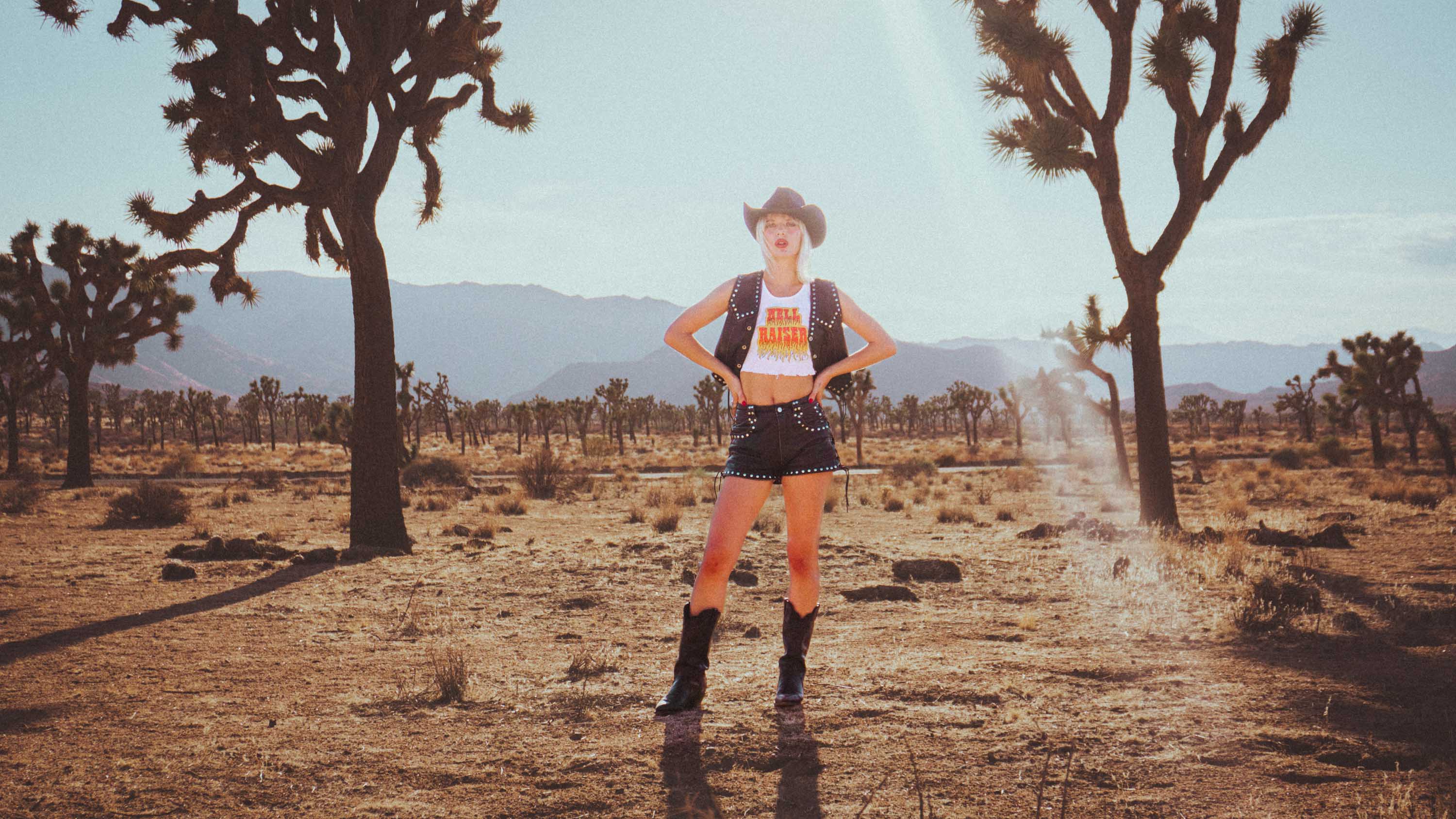 A model wearing Sleazy Rider studded leather and Hell Raiser tank top, standing in Joshua Tree desert.