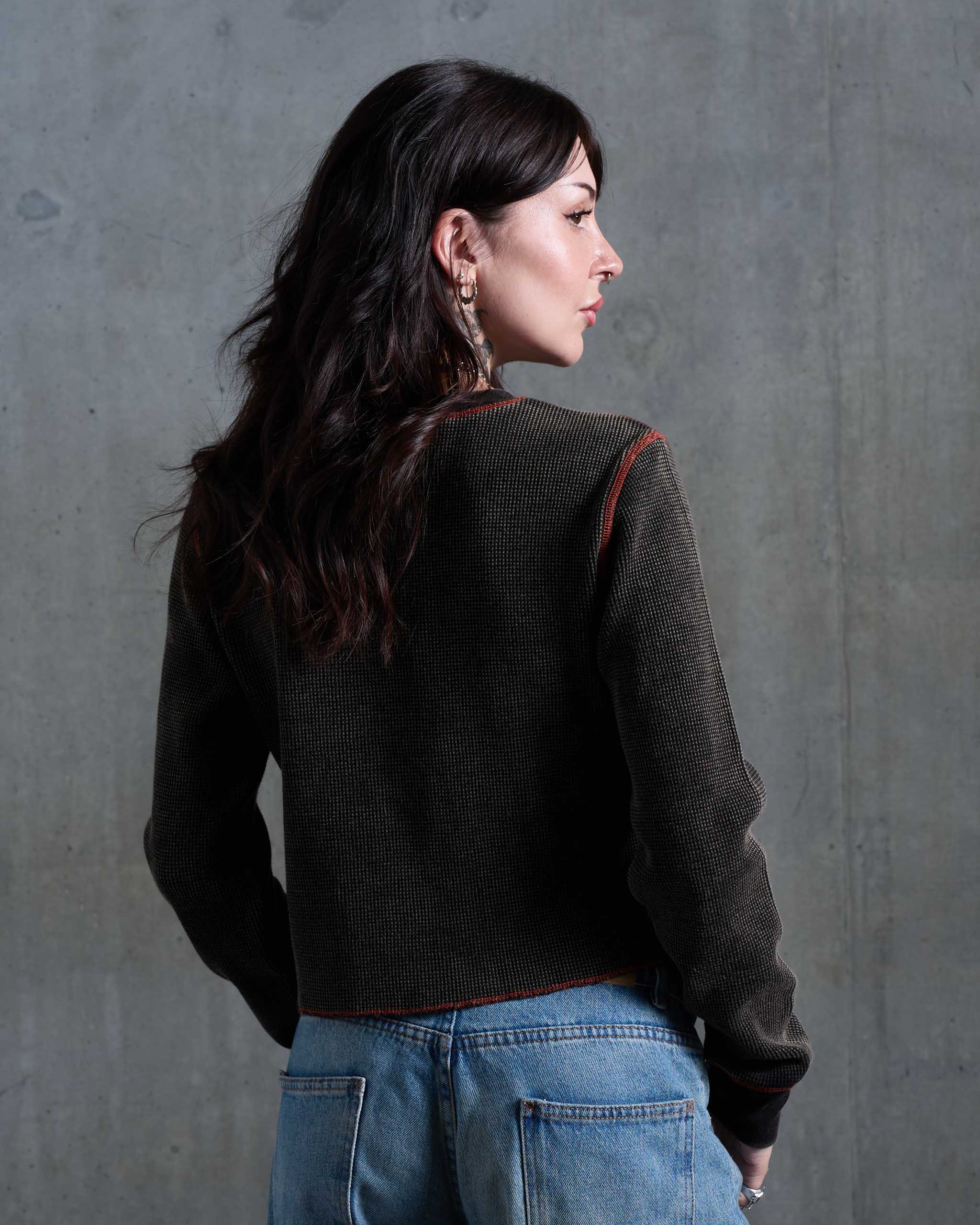A biker woman wearing a dark waffle knit top with orange contrast stitching, view from behind.