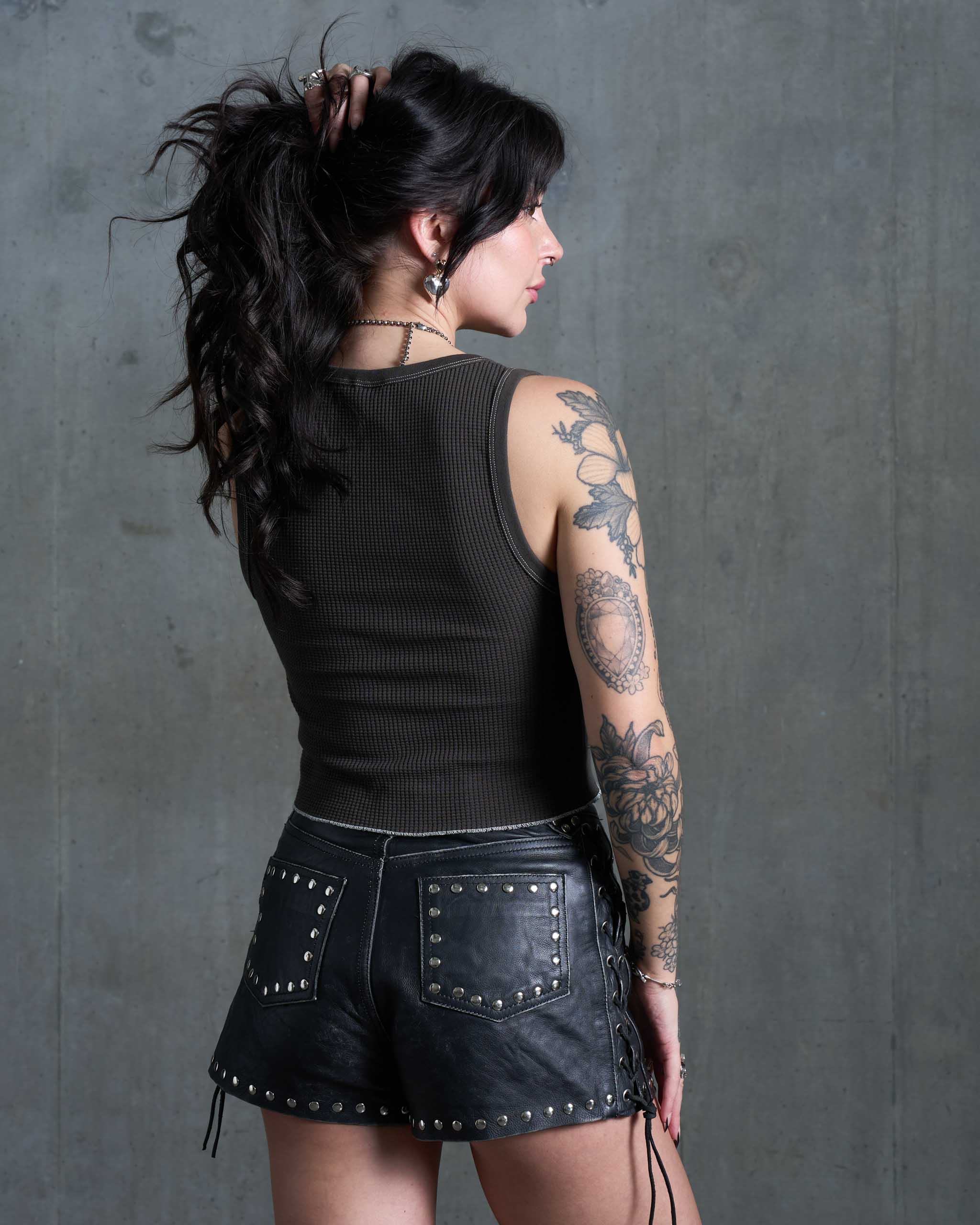 A woman wearing a waffle knit tank top and studded leather shorts.